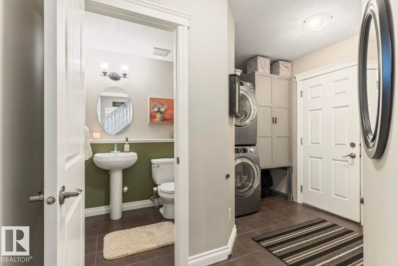 Pedestal sink, wall-mounted light fixture, tile flooring, built-in storage cabinetry, and stacked laundry appliances - 22 Voleta Crest, Spruce Grove, AB