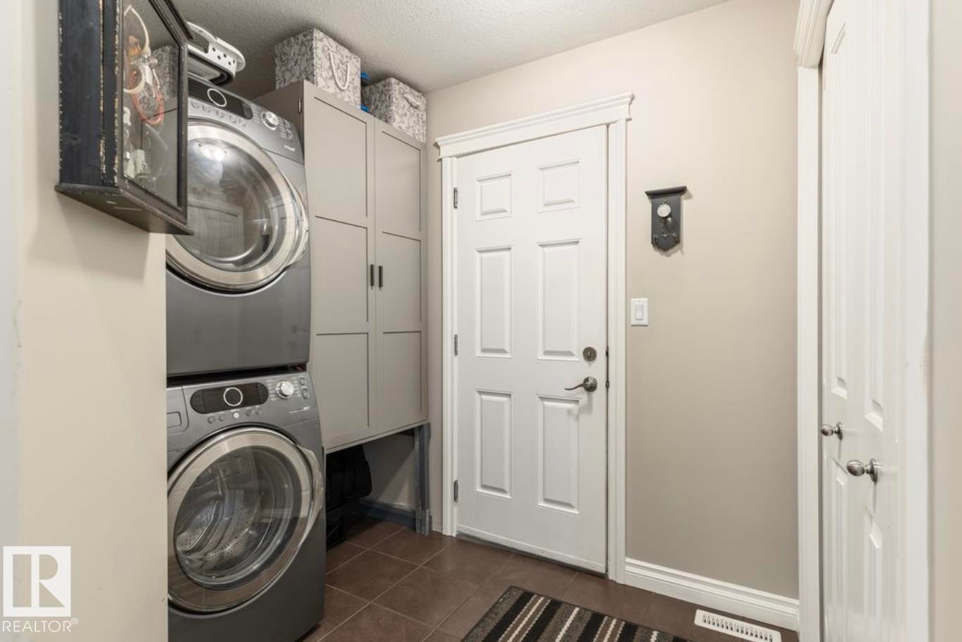 Laundry area featuring stacked appliances, built-in cabinetry, and tile flooring - 22 Voleta Crest, Spruce Grove, AB