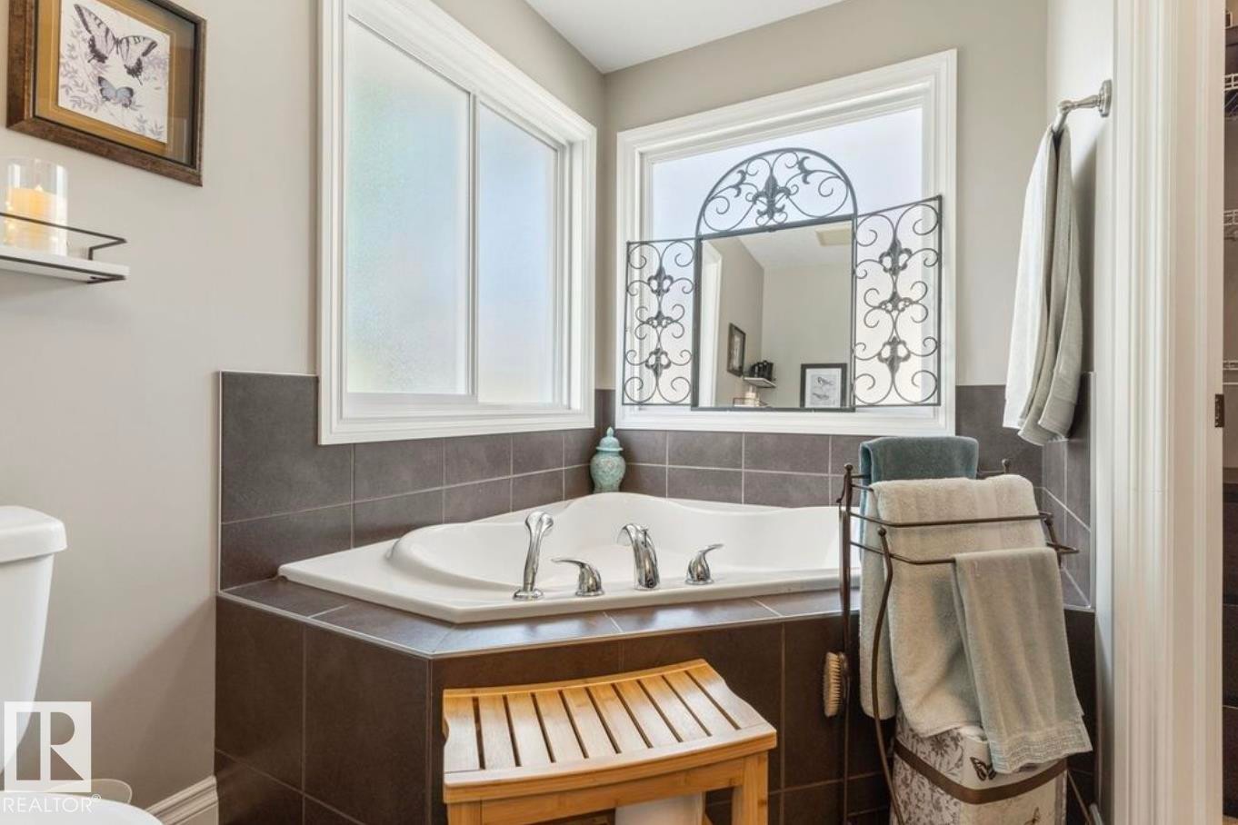 Corner soaking tub with tile surround, two white-framed windows, and an ornate wall-mounted mirror - 22 Voleta Crest, Spruce Grove, AB