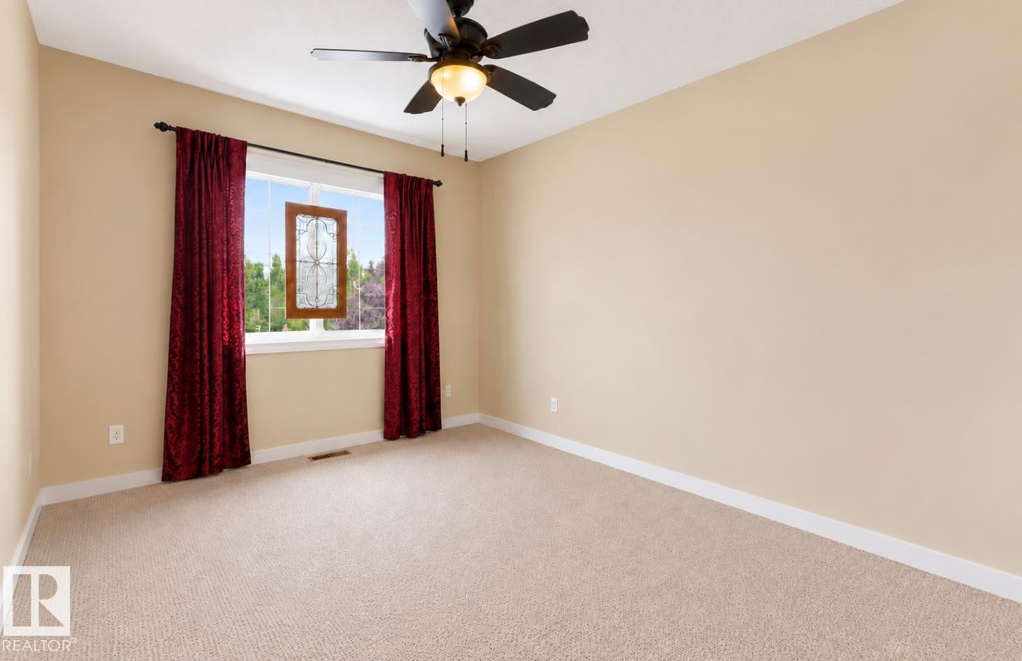 Neutral wall paint, beige carpet, window with intricate wood-framed accent, and a ceiling fan with integrated lighting - 22 Voleta Crest, Spruce Grove, AB