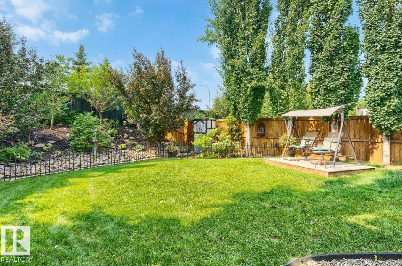 Expansive backyard with a manicured lawn, tiered landscaping, wood fencing, and mature trees - 22 Voleta Crest, Spruce Grove, AB