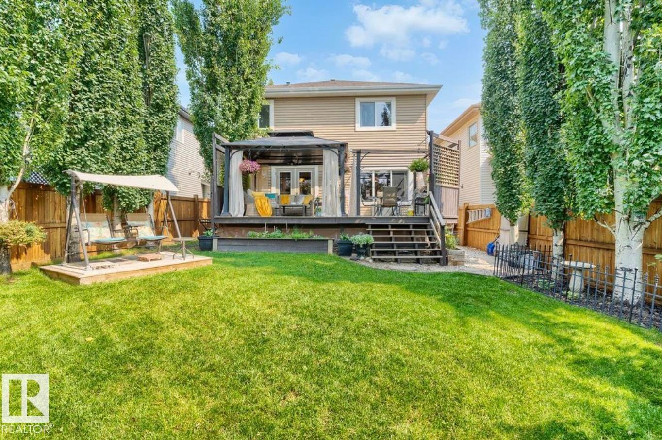 Expansive backyard featuring a manicured lawn, a multi-level wooden deck, and mature trees - 22 Voleta Crest, Spruce Grove, AB