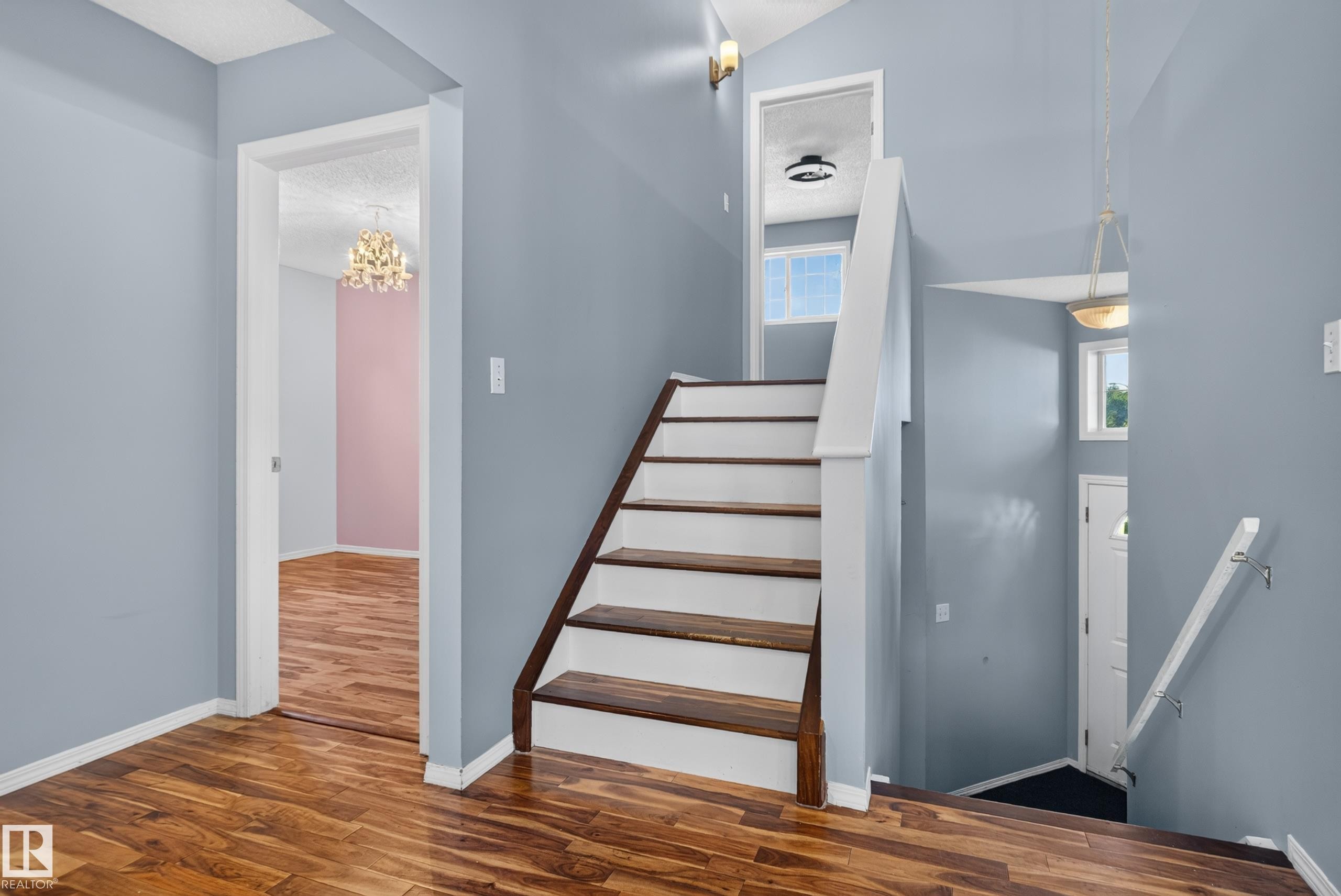 Wood-finish flooring throughout, a two-tone staircase with wood treads and white risers, and a prominent chandelier - 13803 130A Avenue Nw, Edmonton, AB