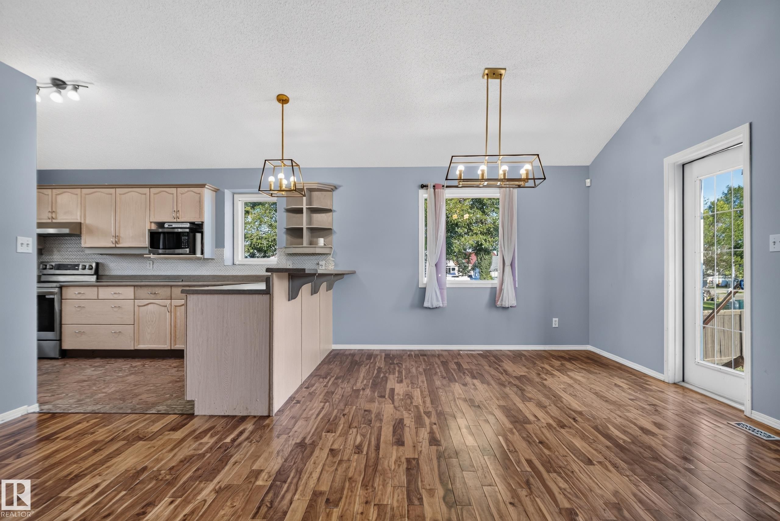 Wood-finish flooring throughout, vaulted ceiling, kitchen featuring light wood cabinetry, stainless steel appliances, and a breakfast bar - 13803 130A Avenue Nw, Edmonton, AB