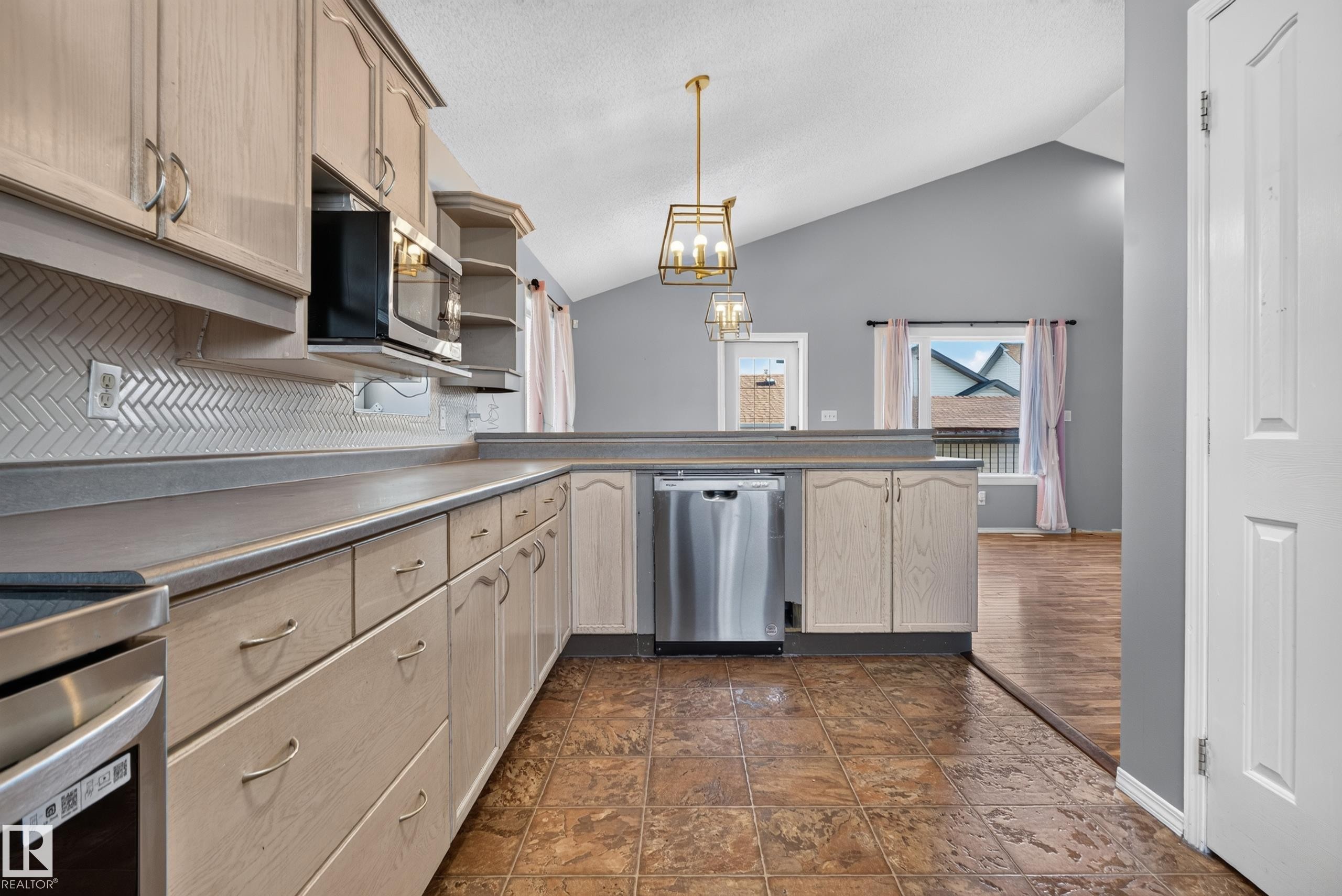 Kitchen featuring stainless steel appliances, herringbone tile backsplash, extensive cabinetry, and a vaulted ceiling - 13803 130A Avenue Nw, Edmonton, AB