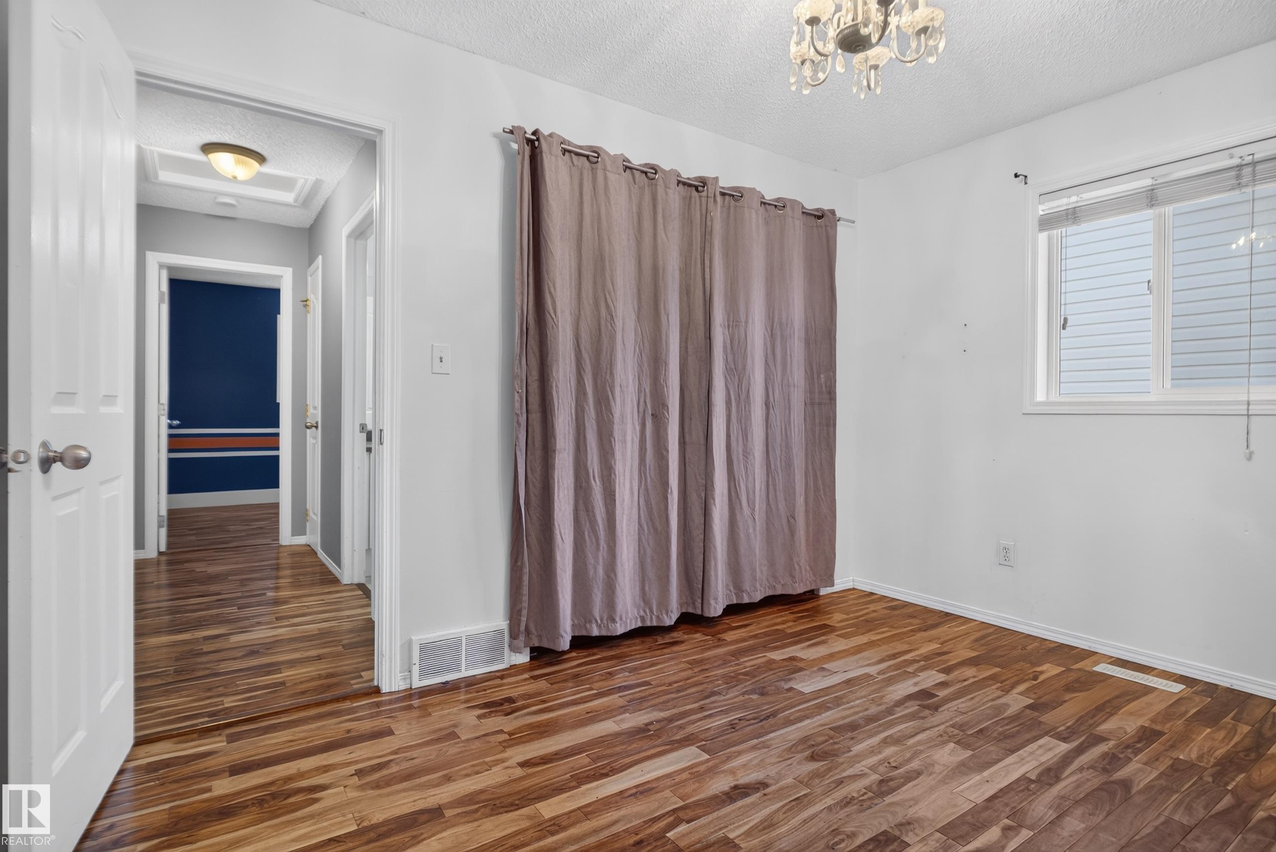 Wood-finish flooring throughout, bright window with blinds, and an overhead chandelier light fixture - 13803 130A Avenue Nw, Edmonton, AB