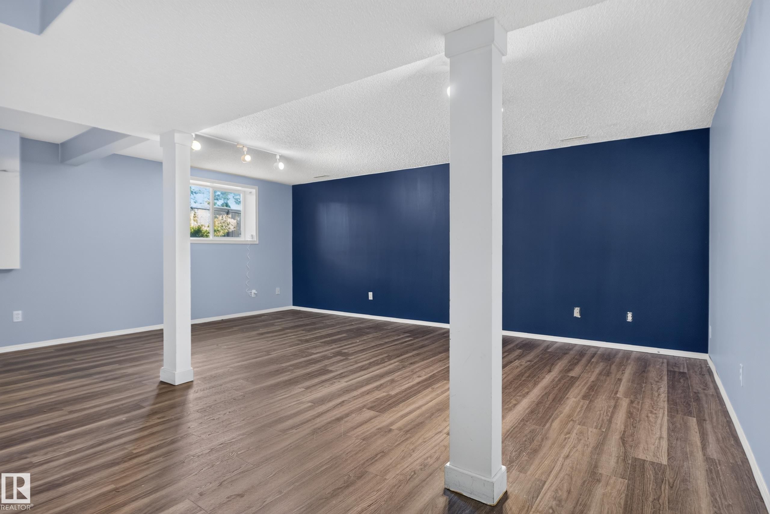 Spacious room featuring wood-finish flooring, light blue and dark blue painted walls, and track lighting - 13803 130A Avenue Nw, Edmonton, AB
