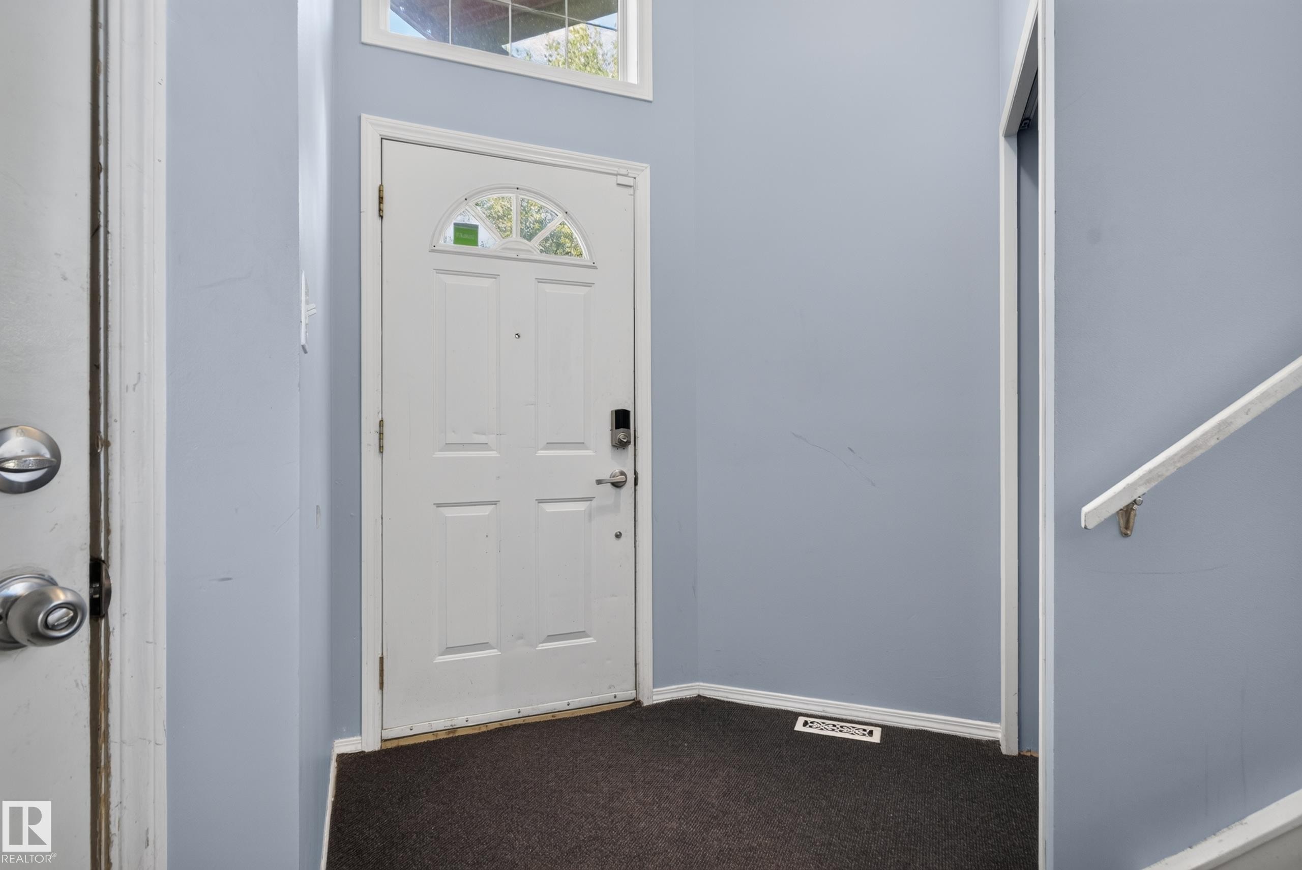 Entryway featuring a white paneled door with an arched glass insert, smart lock hardware, upper transom window, and carpeted flooring - 13803 130A Avenue Nw, Edmonton, AB