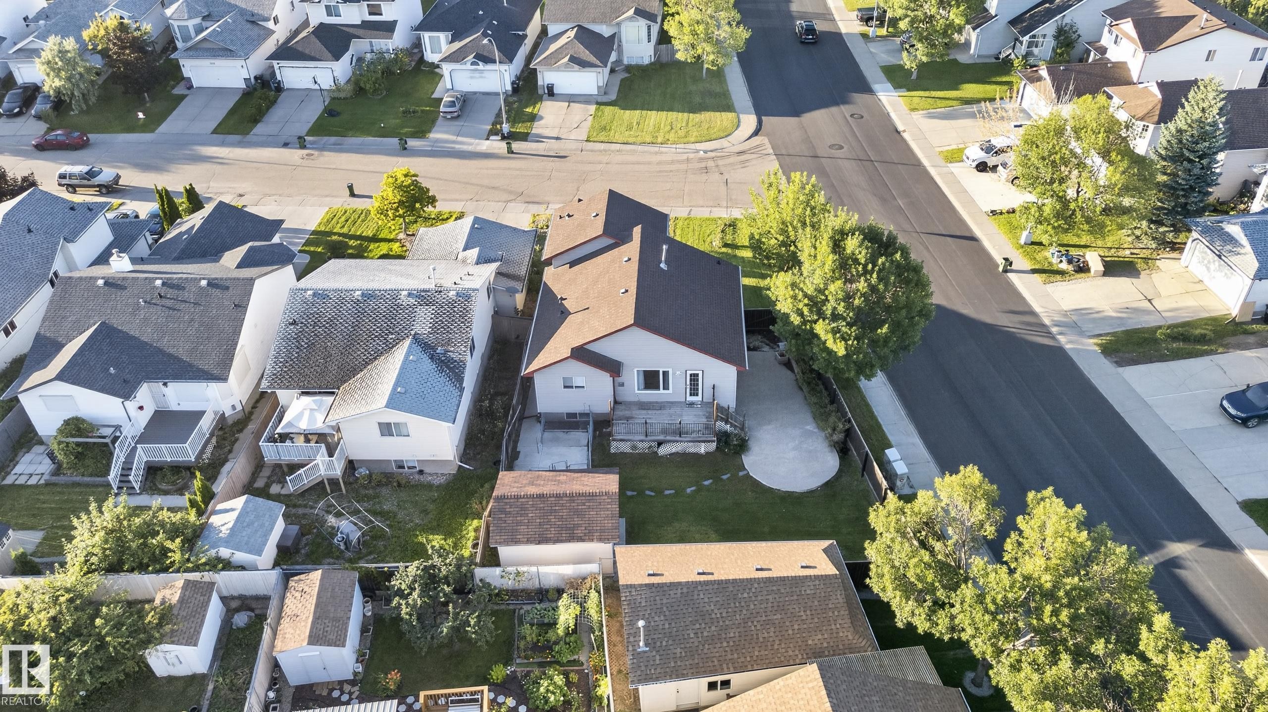 Aerial perspective of a residential property featuring a brown shingle roof, a rear deck, and a concrete patio - 13803 130A Avenue Nw, Edmonton, AB