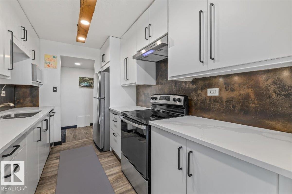 Galley kitchen with white cabinetry, stainless steel appliances, white countertops, and a textured backsplash - #906 12303 Jasper Av Nw, Edmonton, AB