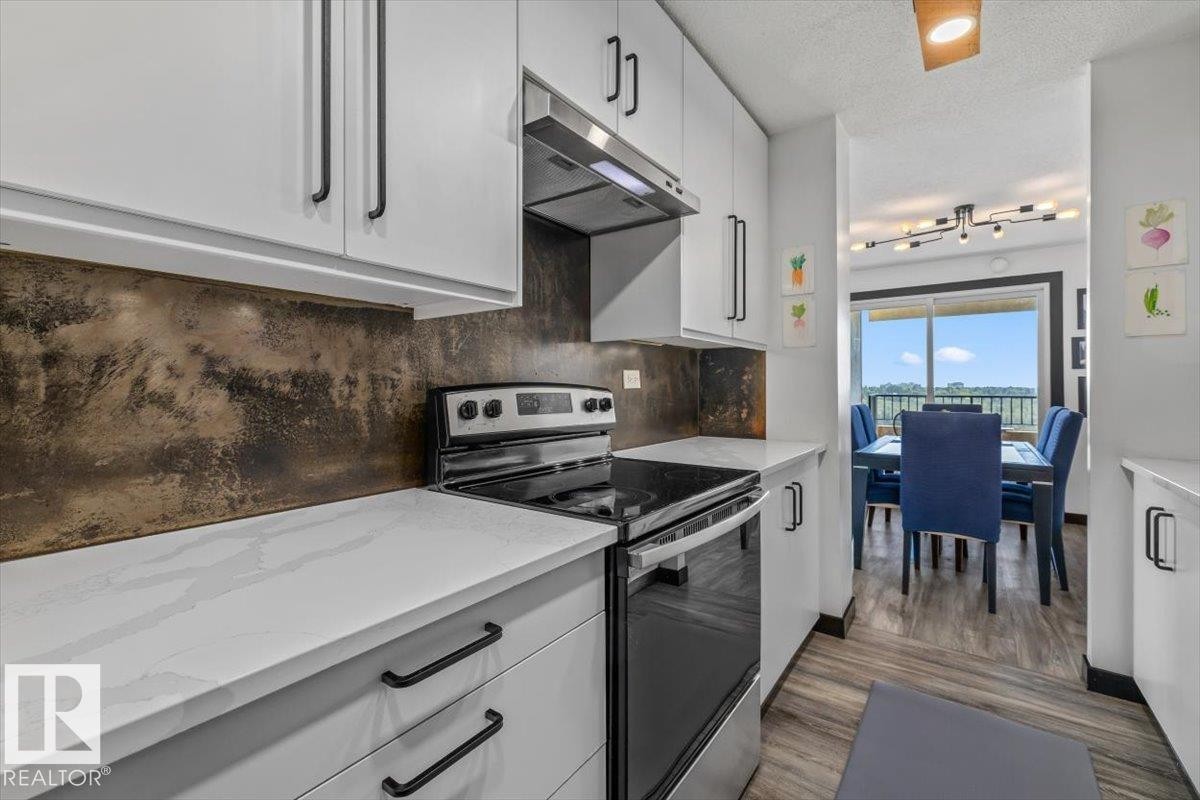 White cabinetry with black hardware, an integrated range hood, white countertops, and a textured backsplash, with wood-finish flooring - #906 12303 Jasper Av Nw, Edmonton, AB