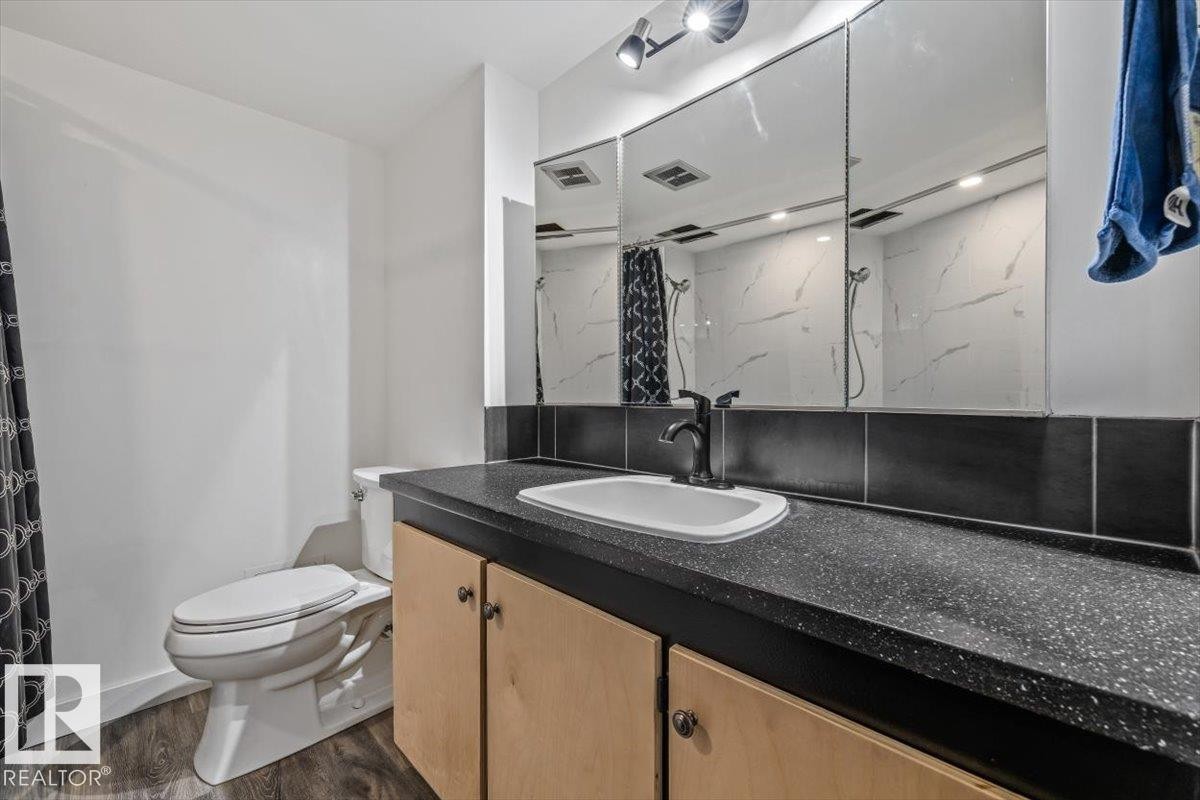 Vanity with integrated sink, black speckled countertop, wood-finish cabinetry, and dark bronze faucet - #906 12303 Jasper Av Nw, Edmonton, AB