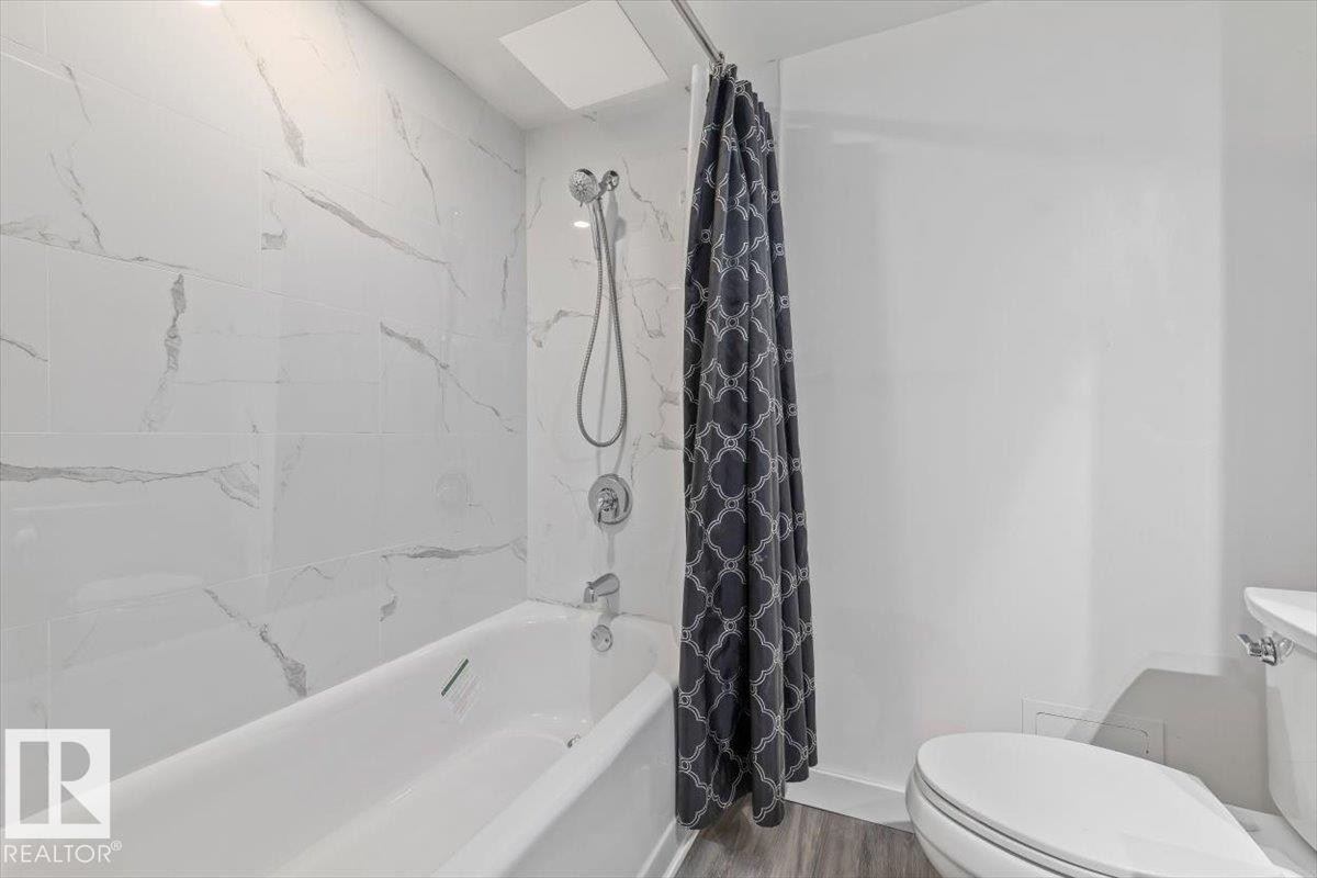 Bathtub with a shower fixture, white tile surround, and wood-finish flooring - #906 12303 Jasper Av Nw, Edmonton, AB