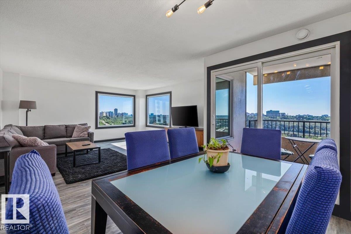 Open-concept living space with wood-finish flooring, multiple windows providing natural light, and a sliding glass door to a private balcony - #906 12303 Jasper Av Nw, Edmonton, AB