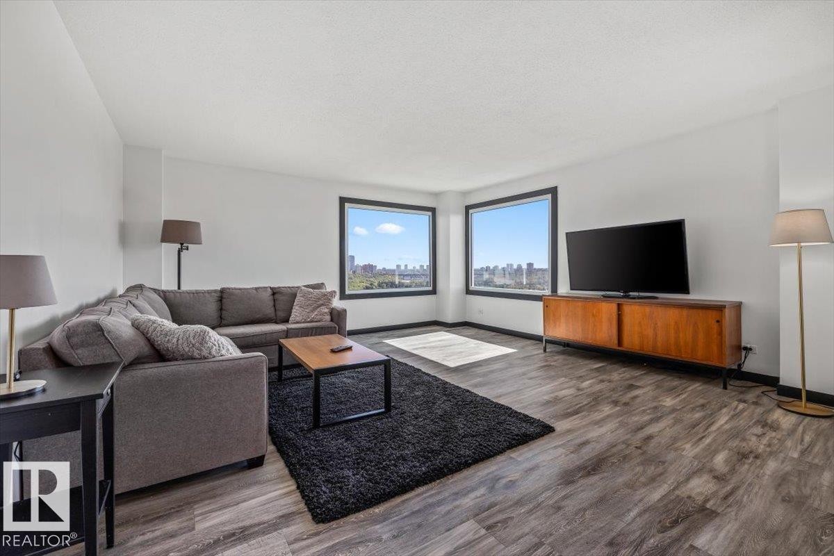 Expansive living area featuring wood-finish flooring, white walls, and multiple large windows with black trim - #906 12303 Jasper Av Nw, Edmonton, AB