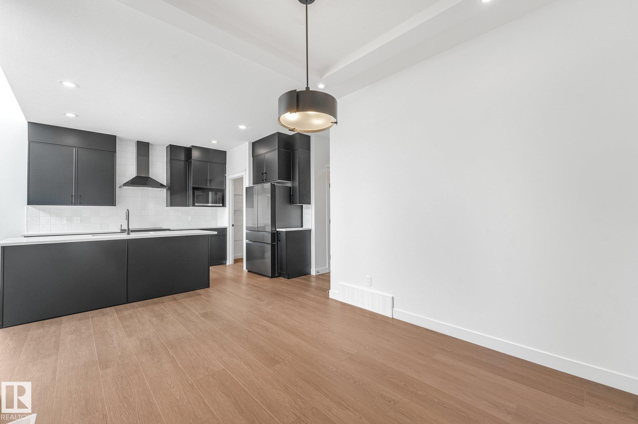 Kitchen featuring an island, integrated sink, matte black cabinetry, a white subway tile backsplash, and stainless steel appliances - 511 157 Avenue Ne, Edmonton, AB