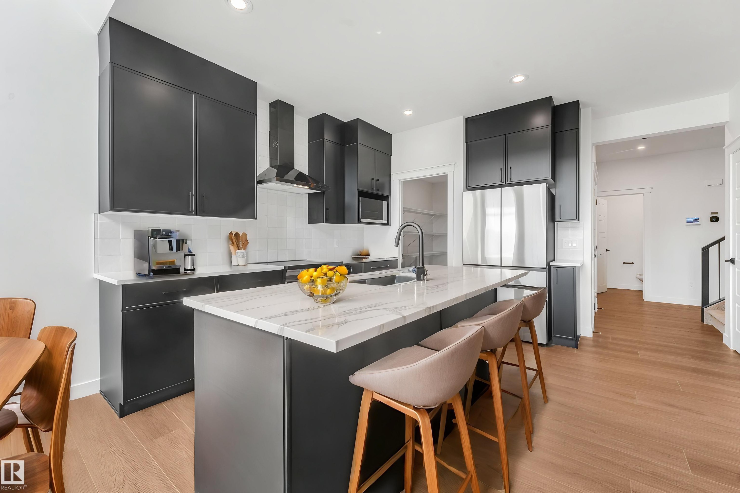 Modern kitchen featuring dark cabinetry, stainless steel appliances, a center island with a stone-finish countertop, and wood-finish flooring - 511 157 Avenue Ne, Edmonton, AB
