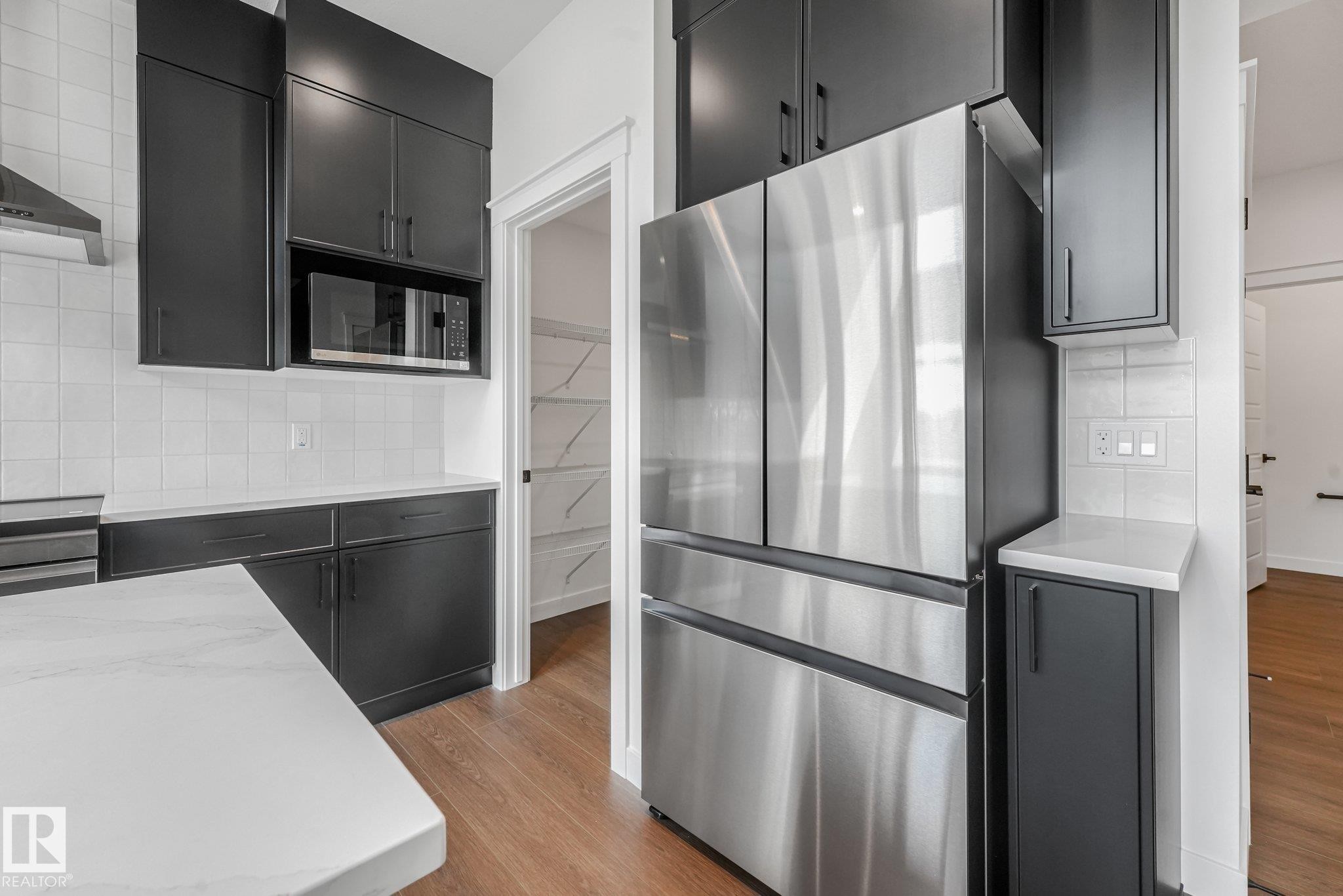 Stainless steel refrigerator, dark cabinetry, white tile backsplash, light countertop, and wood-finish flooring - 511 157 Avenue Ne, Edmonton, AB