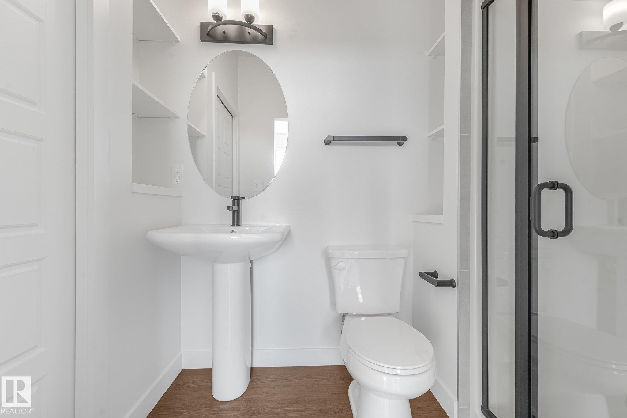 Pedestal sink with an oval mirror, modern black fixtures, and a shower with a black-framed glass door - 511 157 Avenue Ne, Edmonton, AB