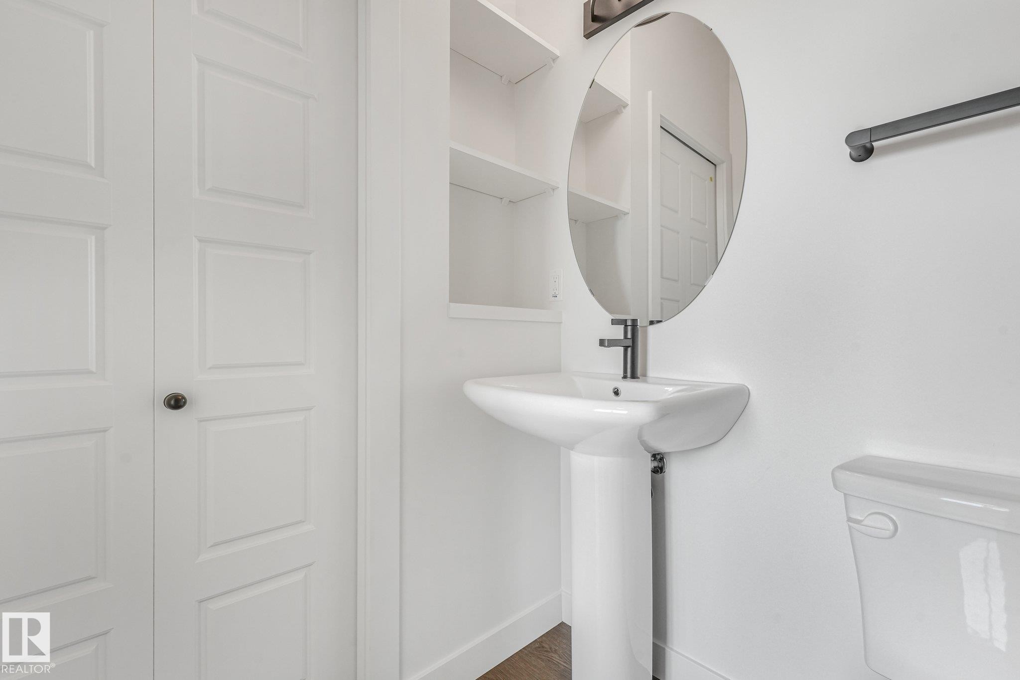 White pedestal sink with a modern faucet, oval mirror, and built-in shelving - 511 157 Avenue Ne, Edmonton, AB