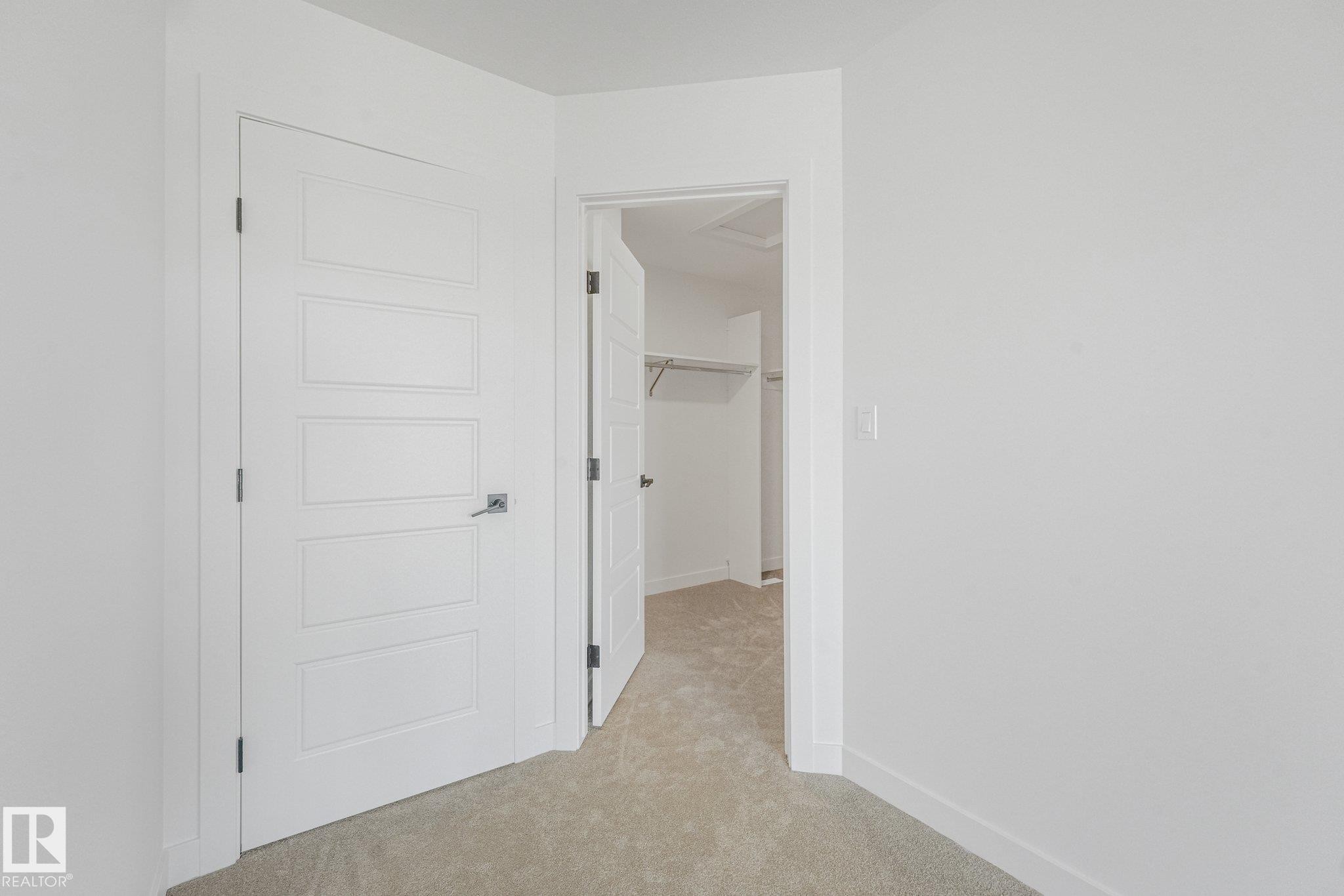 Beige carpeted flooring, white walls, and a modern five-panel interior door with dark hardware - 511 157 Avenue Ne, Edmonton, AB