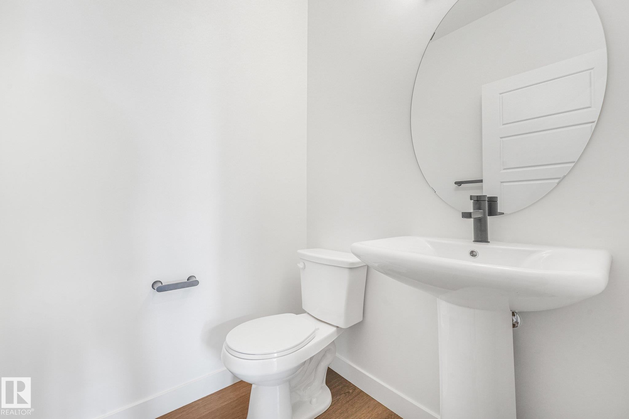 Pedestal sink with matte black faucet, oval mirror, and wood-finish flooring - 511 157 Avenue Ne, Edmonton, AB