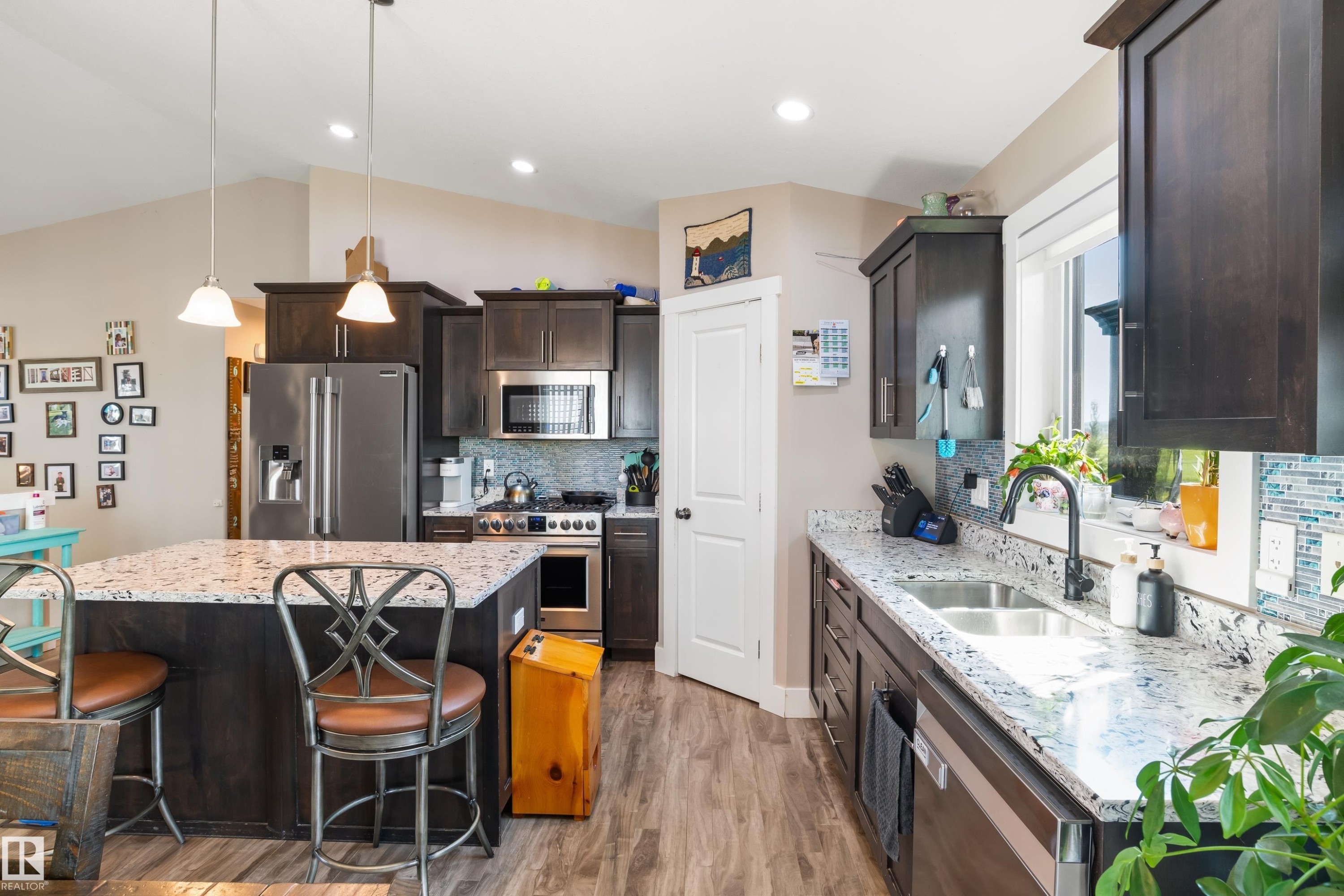 Kitchen featuring dark wood-finish cabinetry, stainless steel appliances, speckled stone countertops, and a tile backsplash - 4927 57 Avenue, Cold Lake, AB
