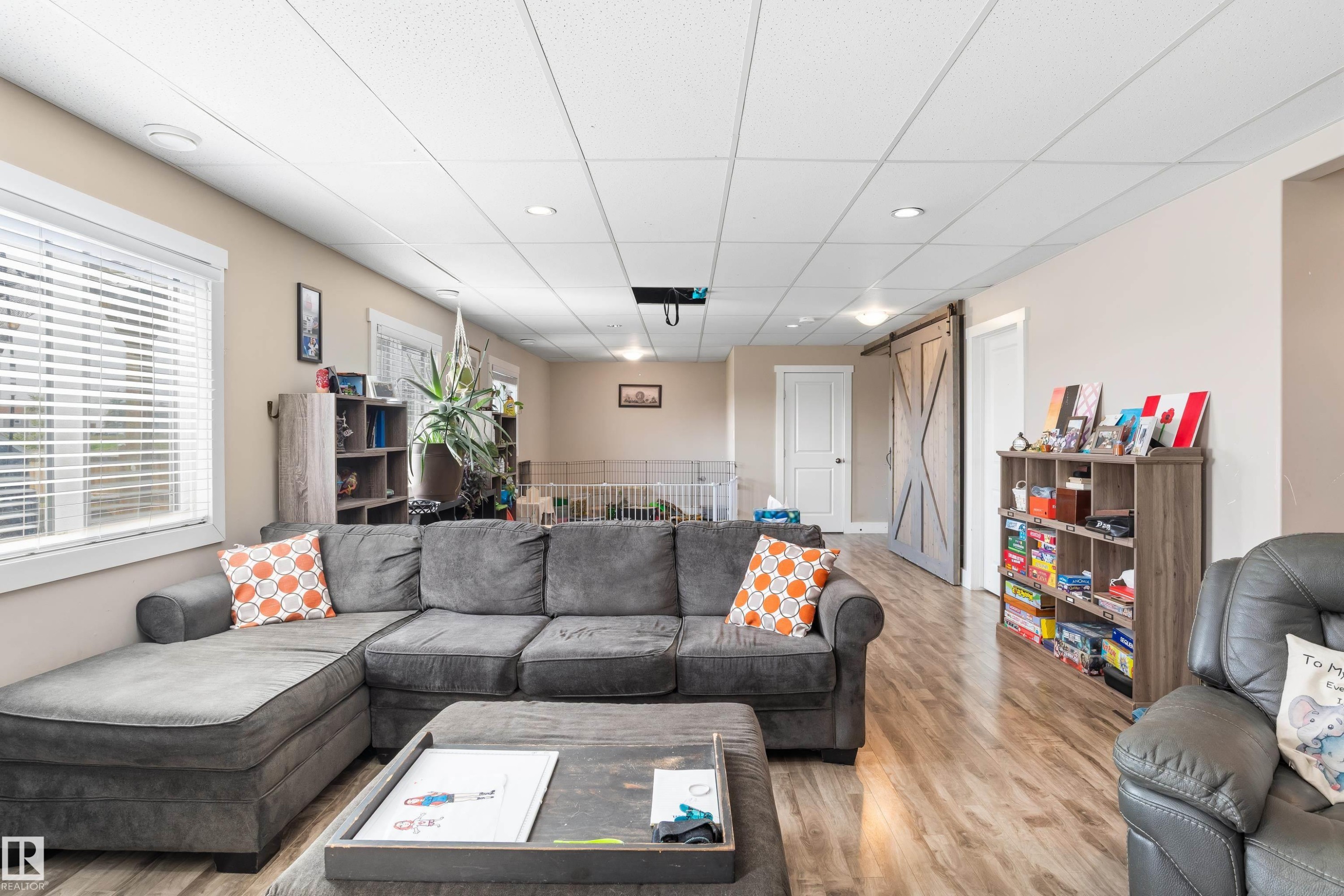 Recessed lighting illuminates the open living area featuring wood-finish flooring, a white window frame, and a barn-style door - 4927 57 Avenue, Cold Lake, AB