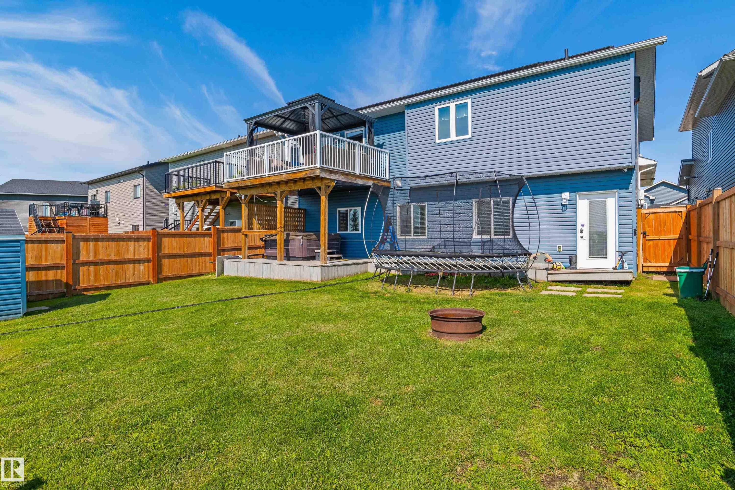 Fenced backyard featuring a manicured lawn, a raised wooden deck with a gazebo, and a lower-level concrete patio - 4927 57 Avenue, Cold Lake, AB