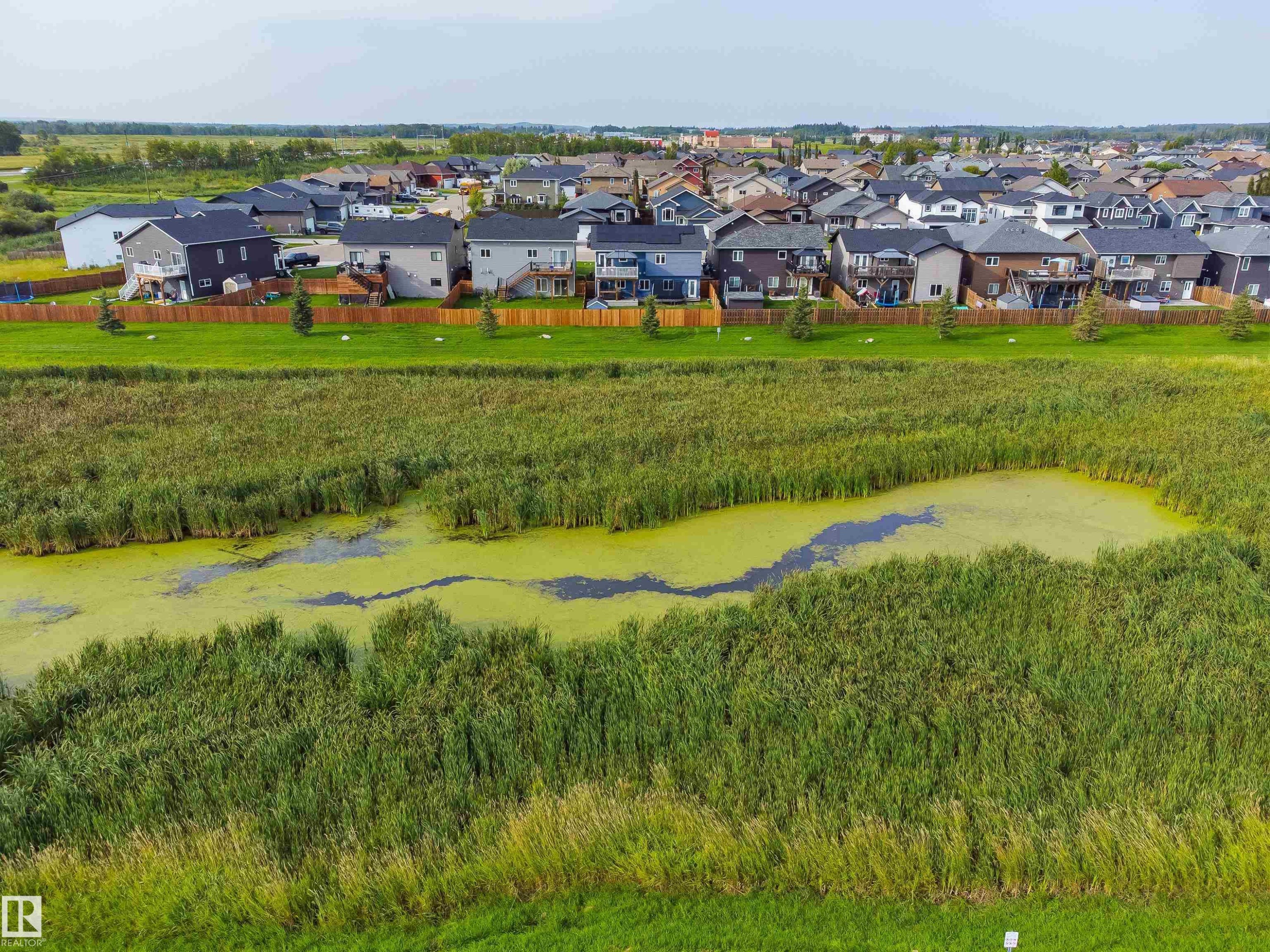Expansive green space featuring a natural pond surrounded by dense vegetation - 4927 57 Avenue, Cold Lake, AB