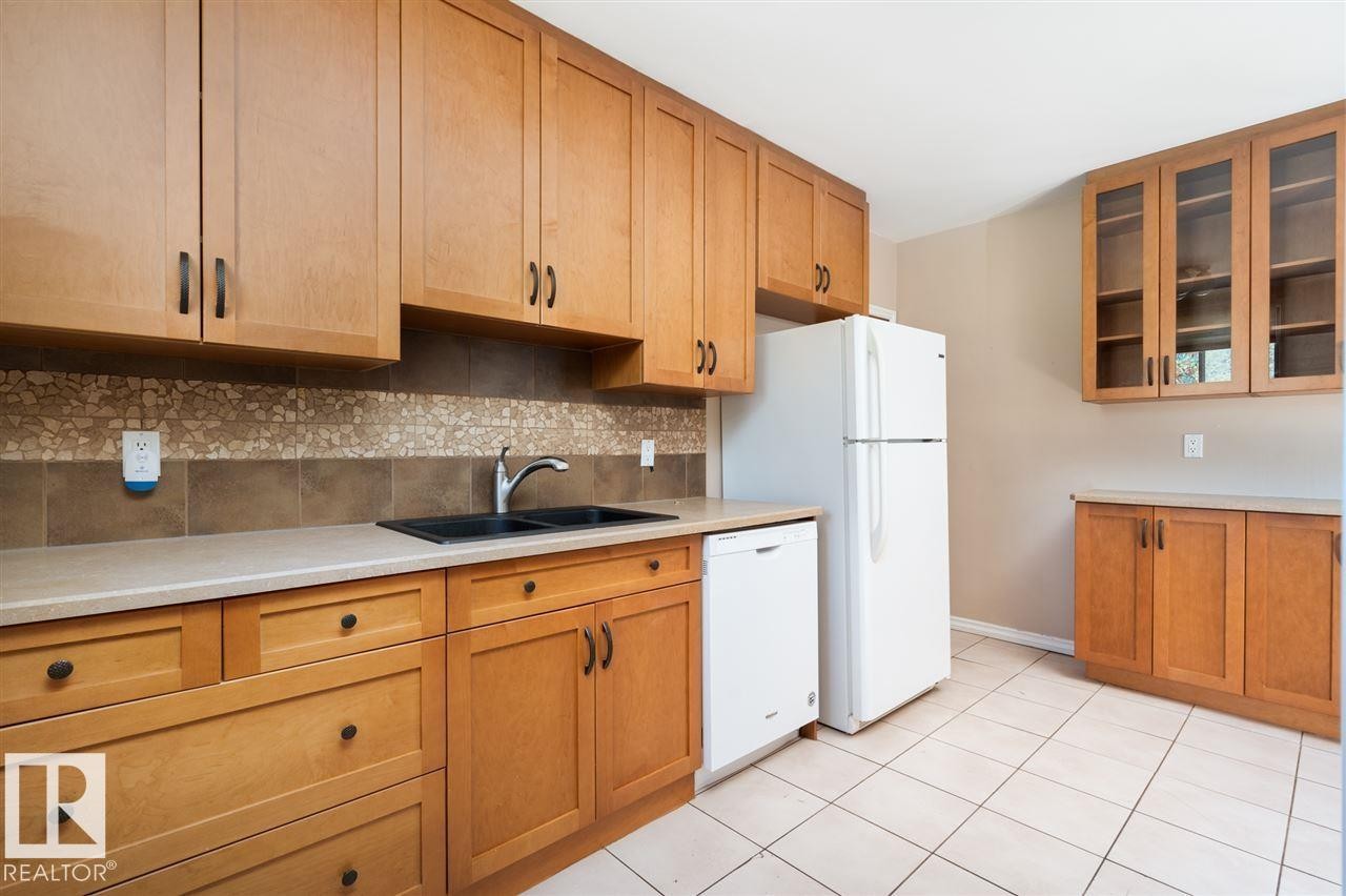Wood-finish cabinetry with dark hardware, dual basin sink with black faucet, light countertops, and tile backsplash - 11730 125 Street Nw, Edmonton, AB