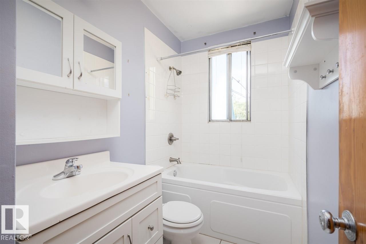 Bathroom featuring a white vanity with integrated sink, white cabinetry with glass inserts, white subway tile surround, and a white bathtub - 11730 125 Street Nw, Edmonton, AB