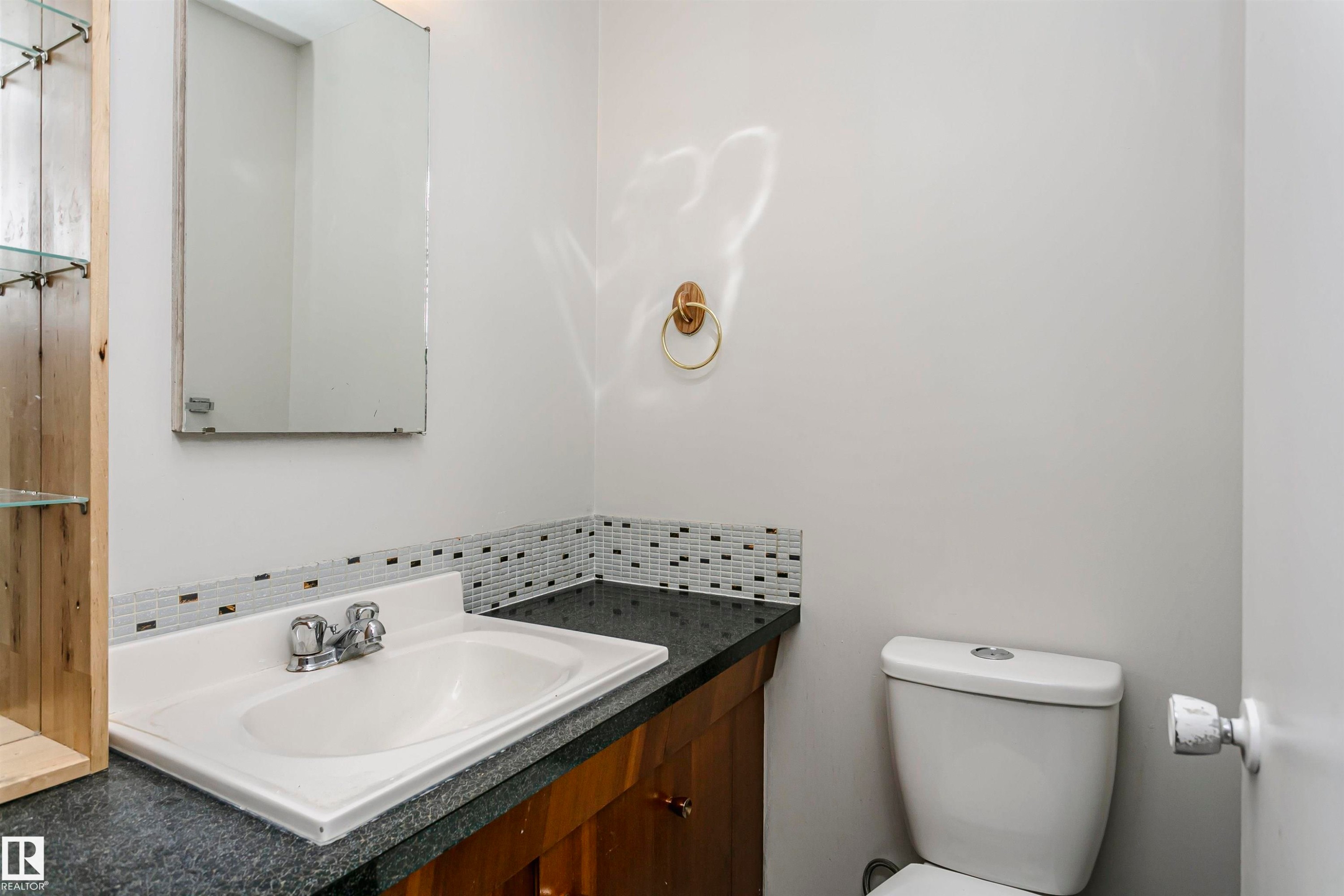 Vanity with a built-in sink, wood-finish cabinetry, dark countertop, and tiled backsplash - 11440 44A Avenue Nw, Edmonton, AB