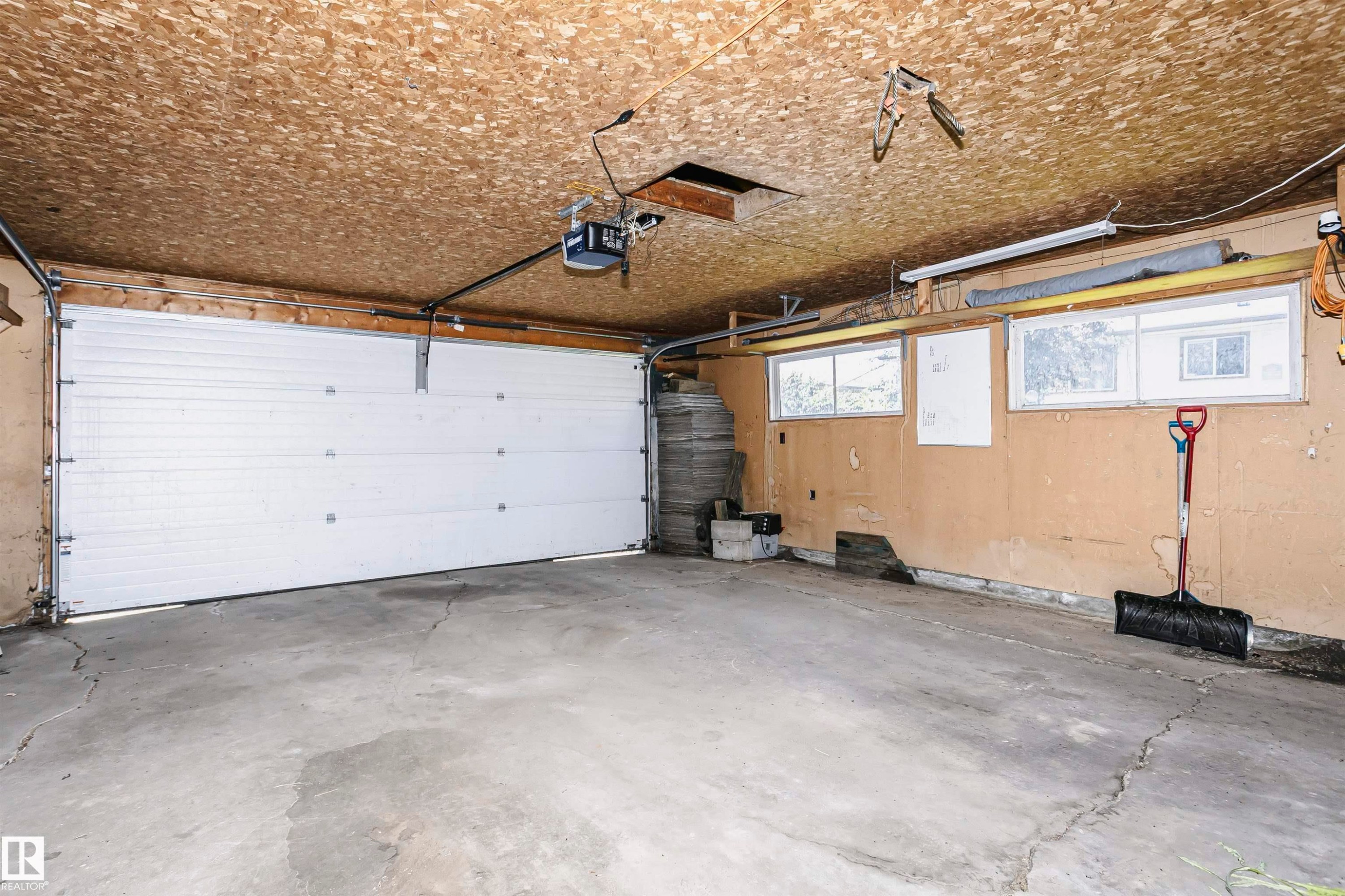 Spacious garage with concrete flooring, overhead door with modern hardware, and exposed beam ceiling - 11440 44A Avenue Nw, Edmonton, AB