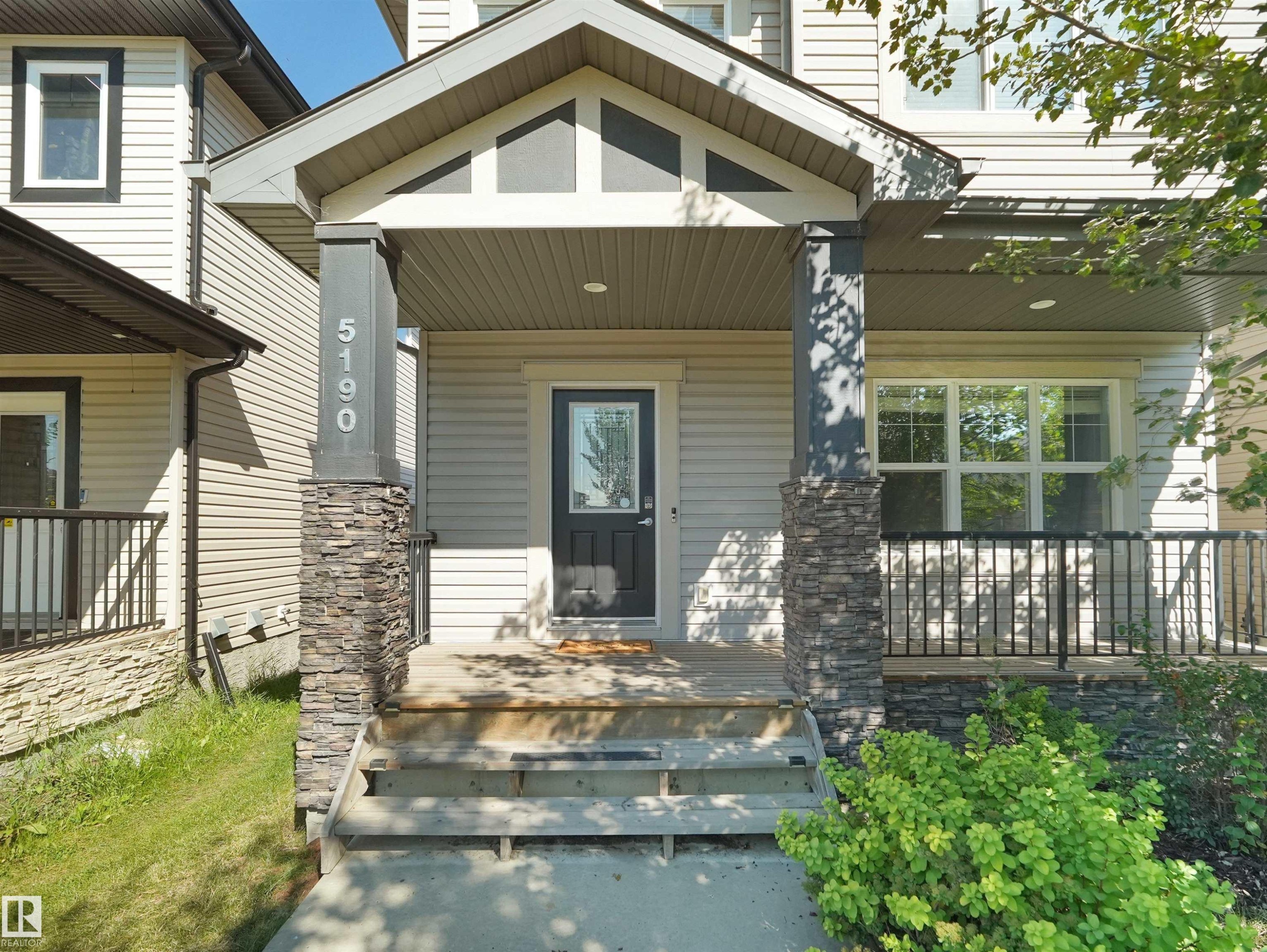 Covered entry with stone-clad columns, white siding, and a dark entry door with decorative glass - 5190 1B Avenue Sw, Edmonton, AB