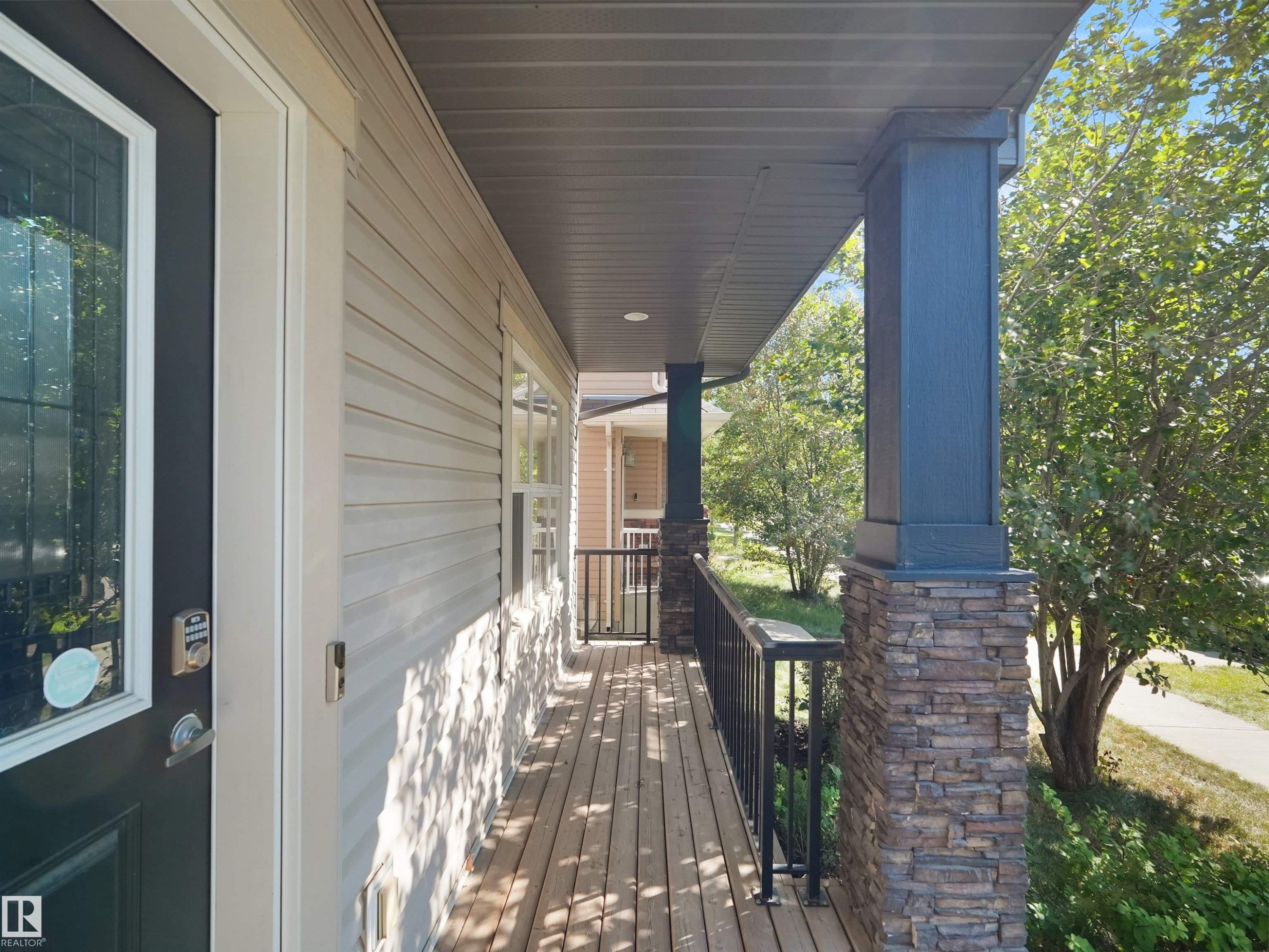Covered porch with wood-finish decking, stone-clad support columns, and black metal railing - 5190 1B Avenue Sw, Edmonton, AB