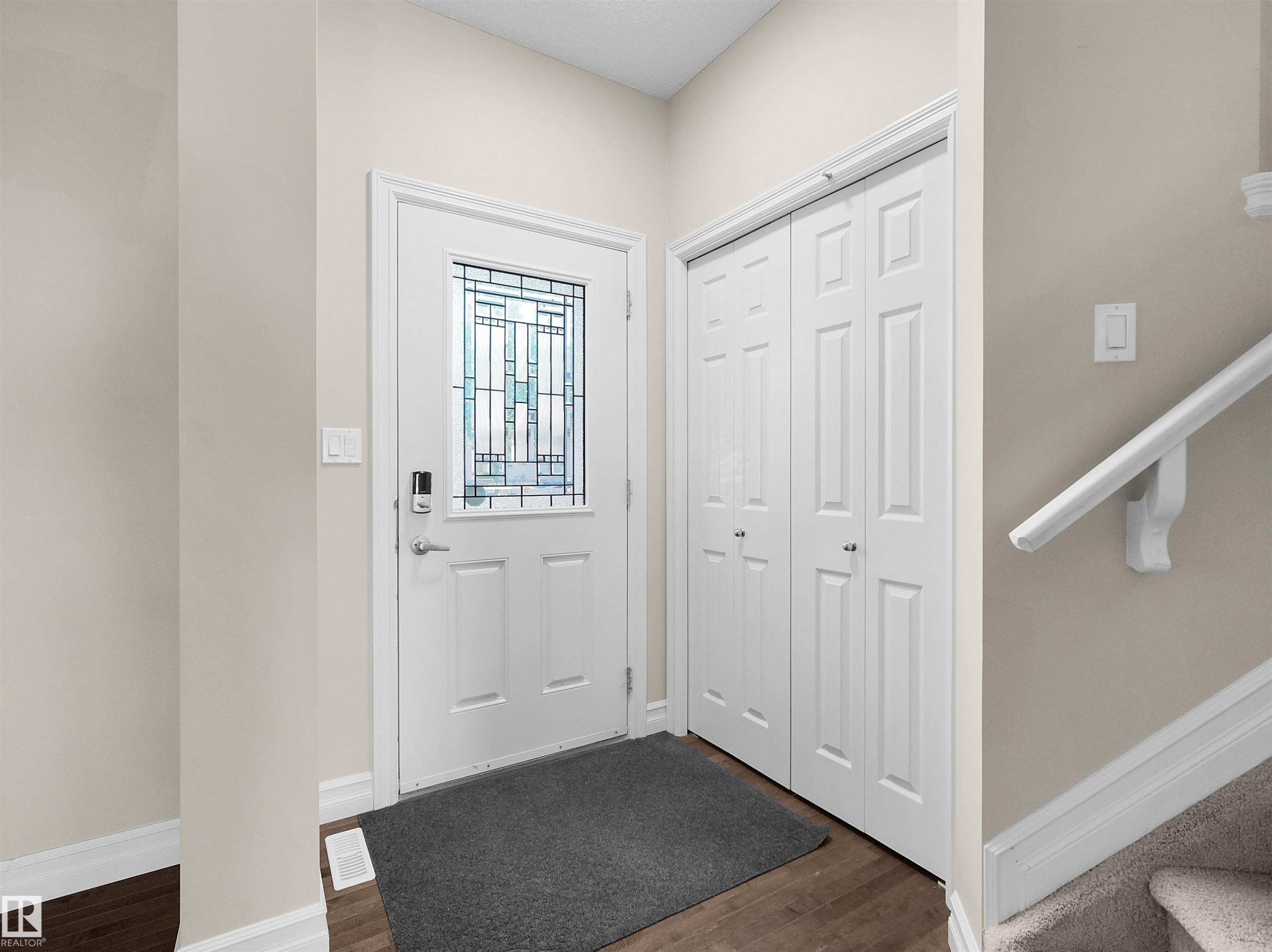 Entryway featuring a white paneled door with decorative glass, wood-finish flooring, and white bi-fold closet doors - 5190 1B Avenue Sw, Edmonton, AB
