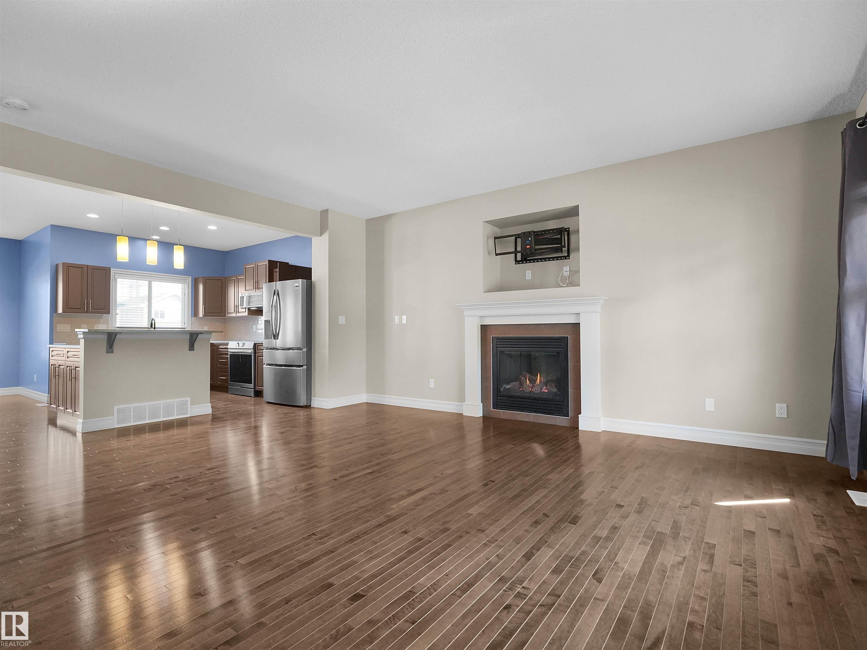 Hardwood-finish flooring throughout, featuring a gas fireplace with a white mantel, and an open-concept kitchen with a breakfast bar and stainless steel appliances - 5190 1B Avenue Sw, Edmonton, AB