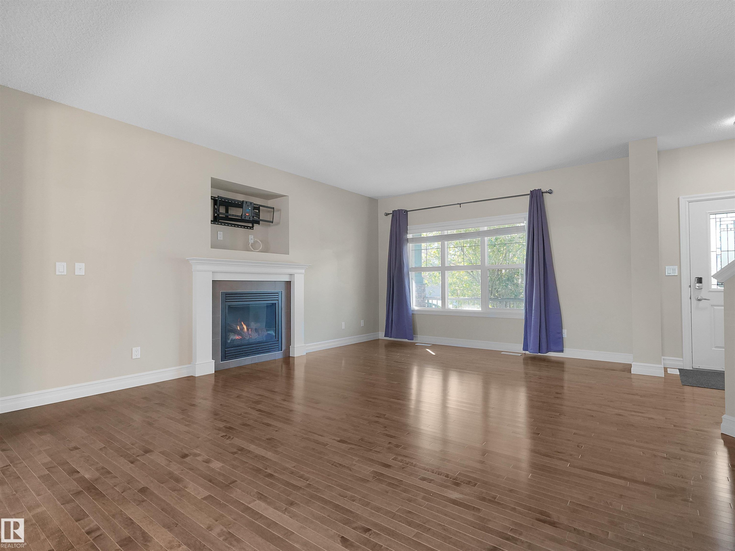 Wood-finish flooring, built-in fireplace with a mantel, recessed niche, and a large window - 5190 1B Avenue Sw, Edmonton, AB