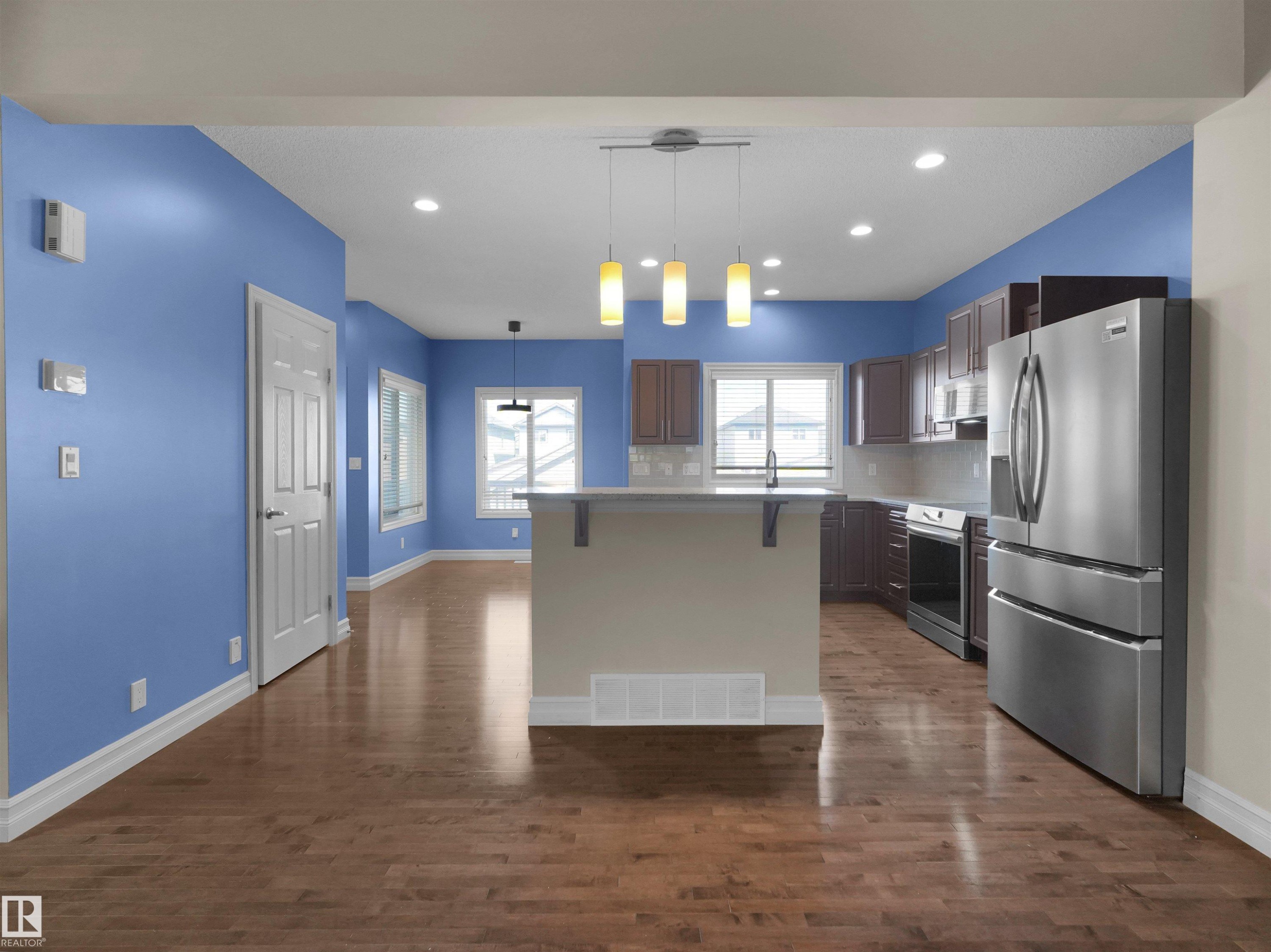 Open-concept kitchen and living area featuring wood-finish flooring, stainless steel appliances, dark wood cabinetry, and recessed lighting - 5190 1B Avenue Sw, Edmonton, AB