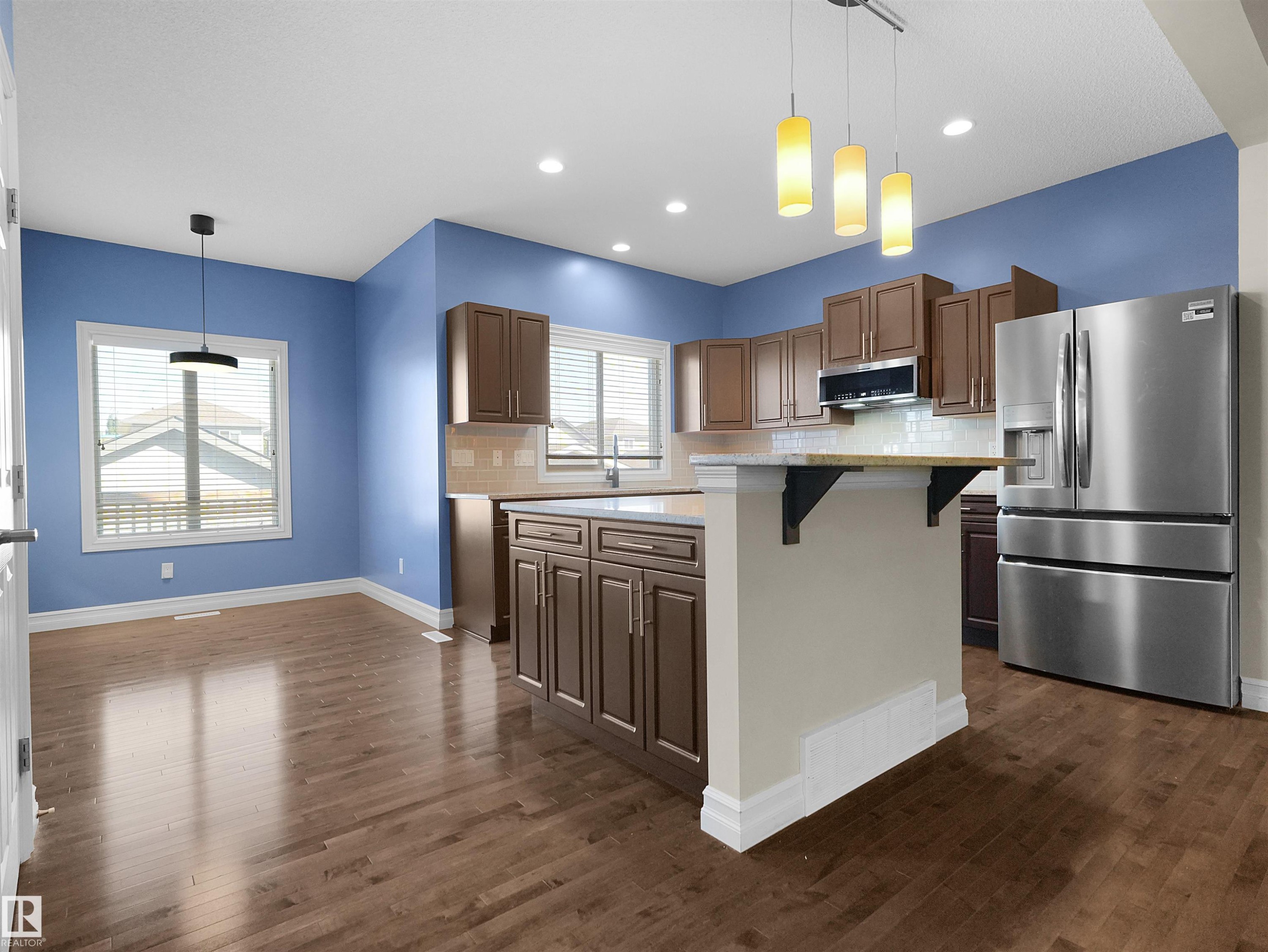 Wood-finish flooring throughout, kitchen with wood cabinetry, stainless steel appliances, and an island with an extended countertop - 5190 1B Avenue Sw, Edmonton, AB