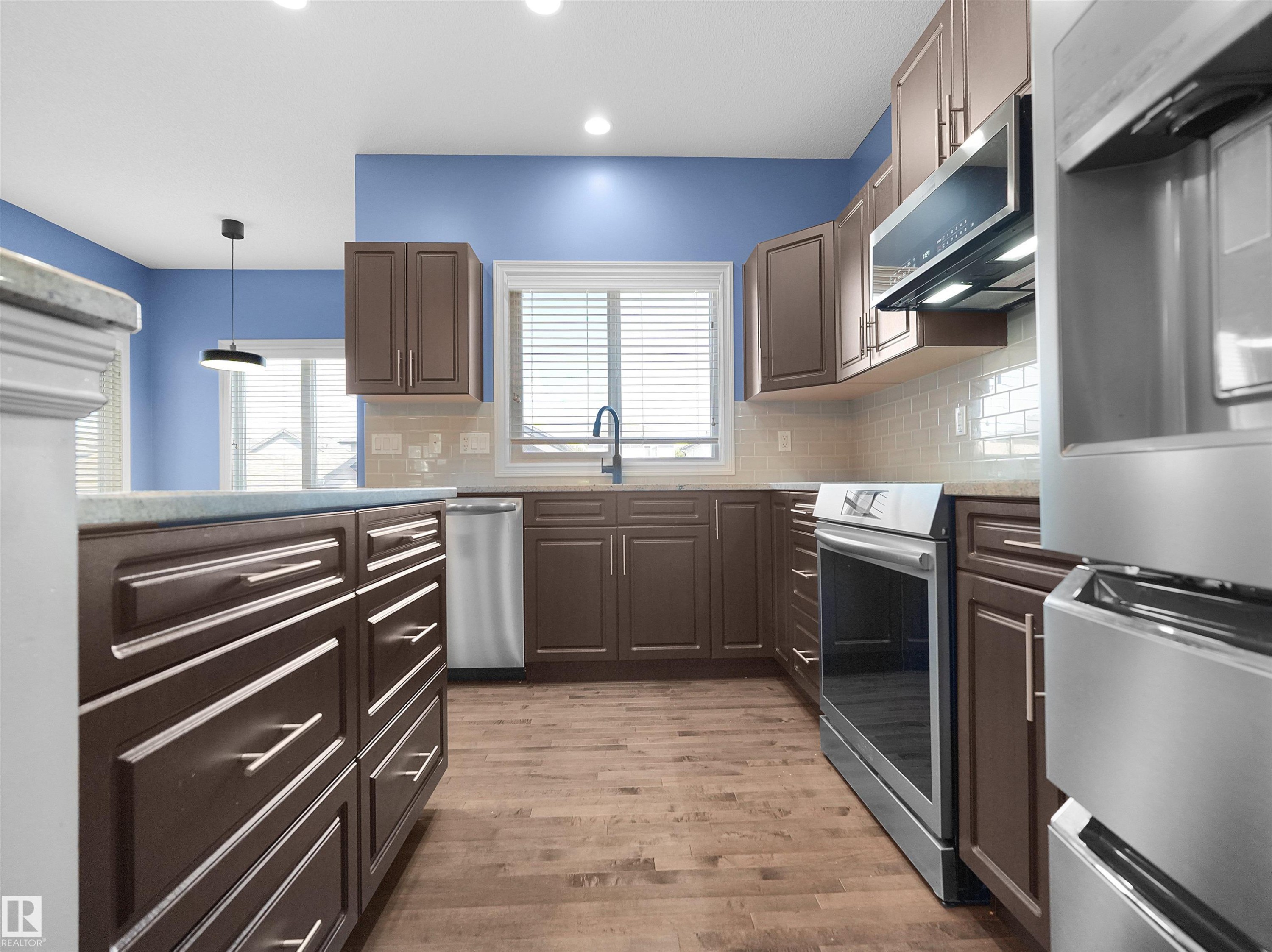 Kitchen featuring wood-finish flooring, dark wood cabinetry, stainless steel appliances, and a tile backsplash - 5190 1B Avenue Sw, Edmonton, AB