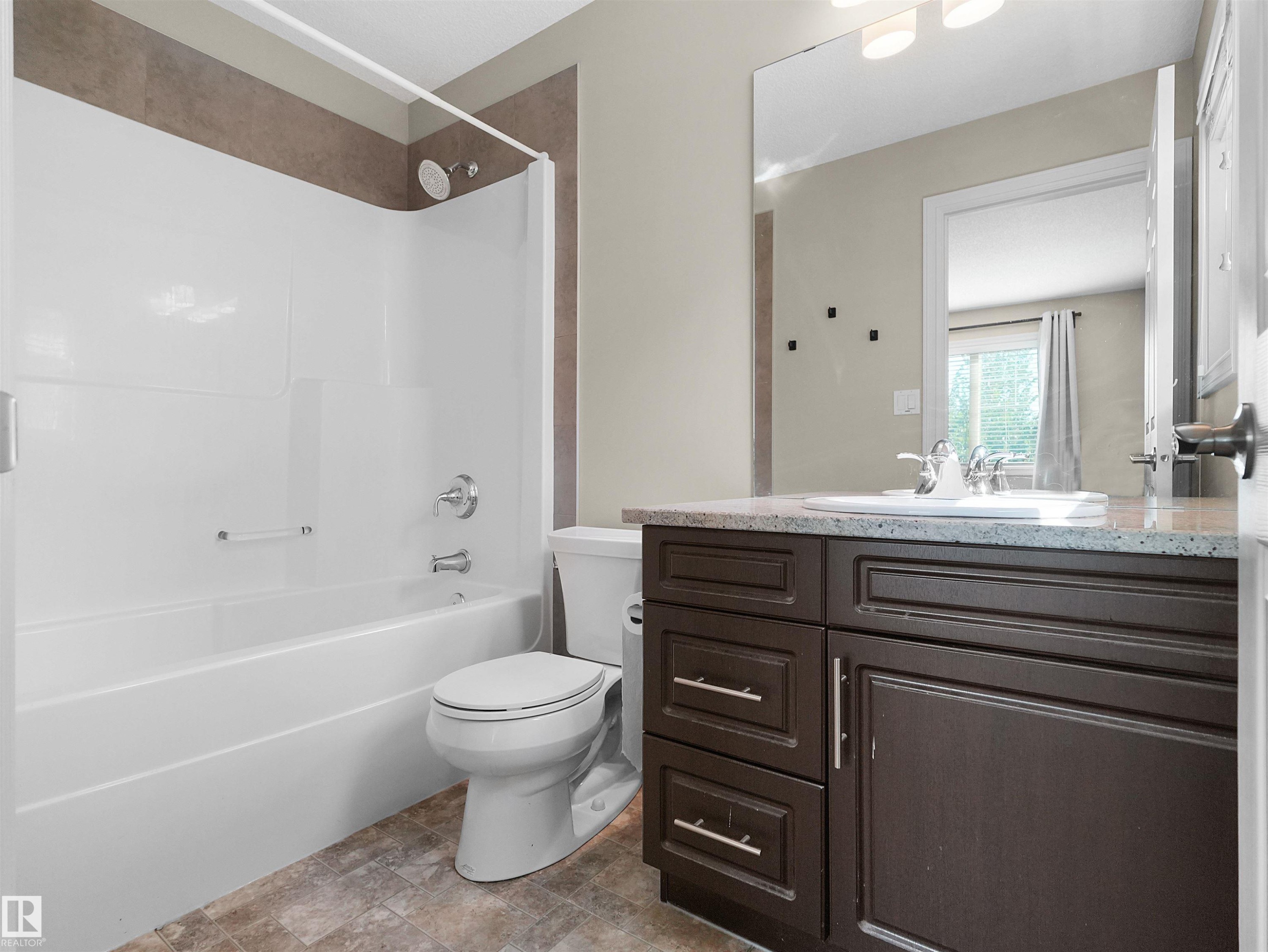 Full bathroom featuring a dark wood-finish vanity with a granite-style countertop, integrated sink, and an expansive wall mirror - 5190 1B Avenue Sw, Edmonton, AB