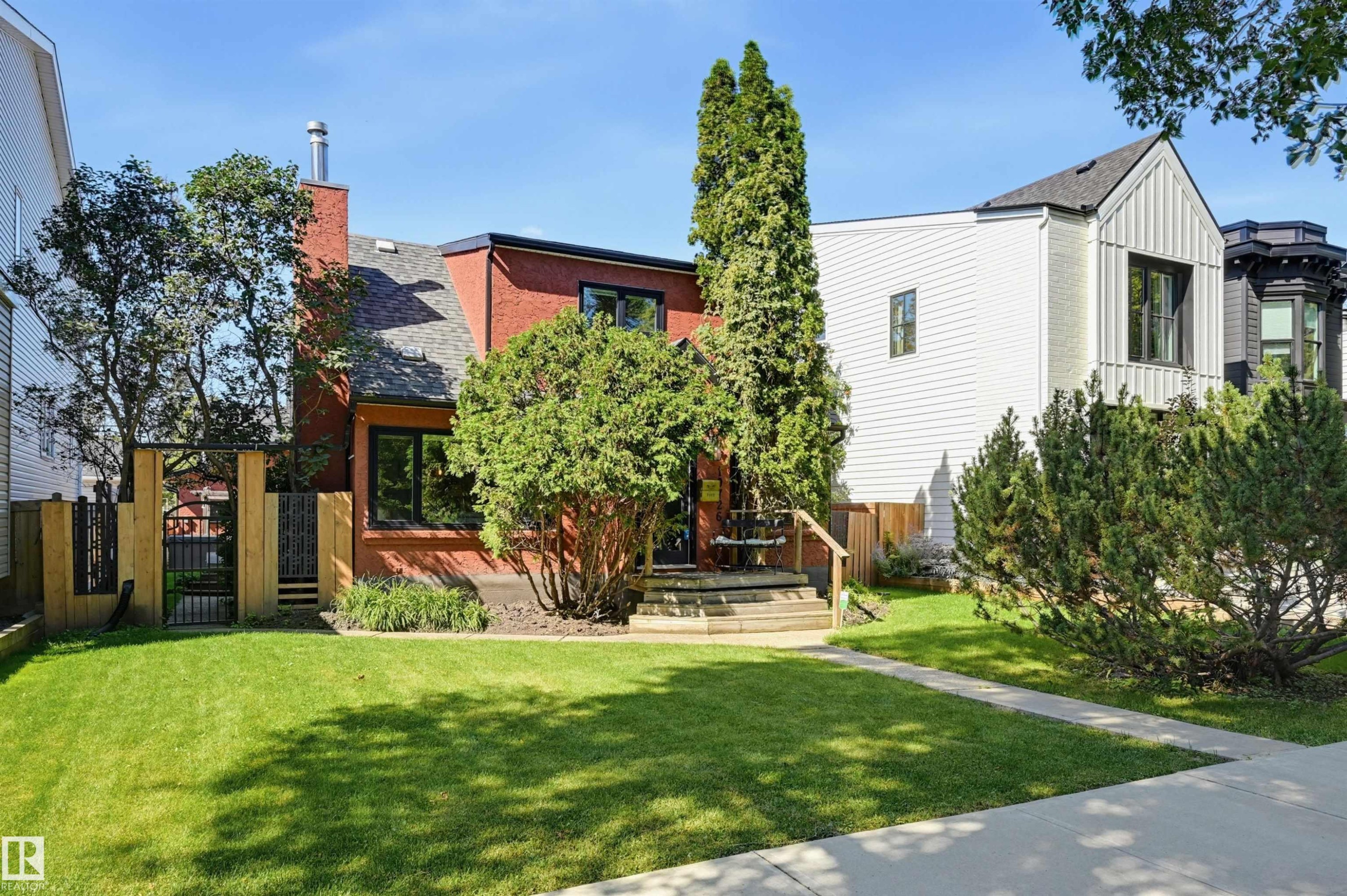 Red brick exterior with dark trim windows, front lawn, mature trees, and a concrete walkway - 10726 128 Street Nw, Edmonton, AB