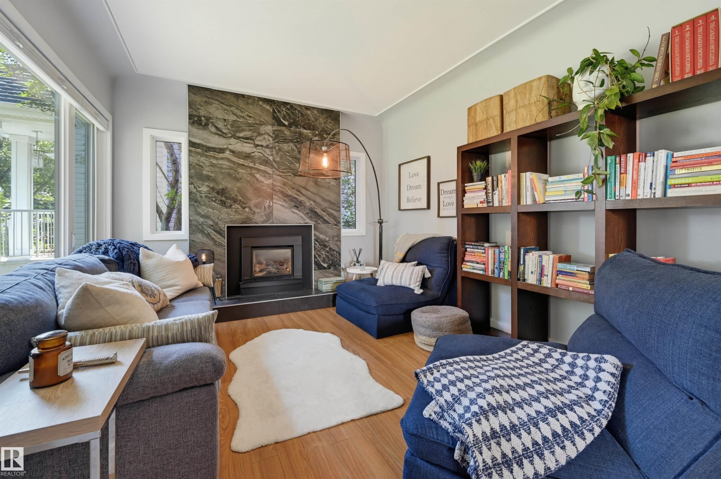 Living area featuring a stone accent wall with a built-in fireplace, wood-finish flooring, large windows, and built-in shelving - 10726 128 Street Nw, Edmonton, AB