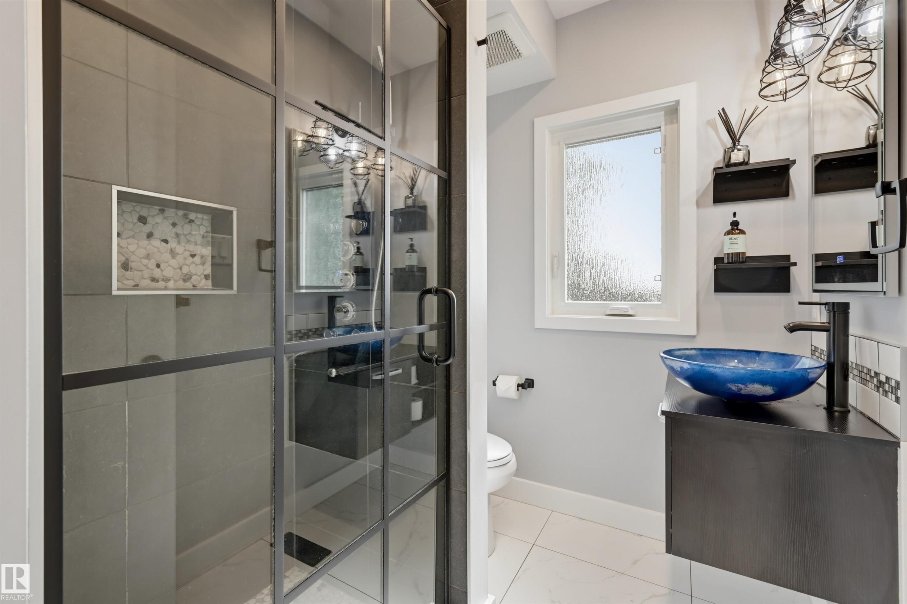 Glass-enclosed shower with black framing, vanity with a vessel sink, black wall-mounted faucet, and overhead cage-style lighting - 10726 128 Street Nw, Edmonton, AB