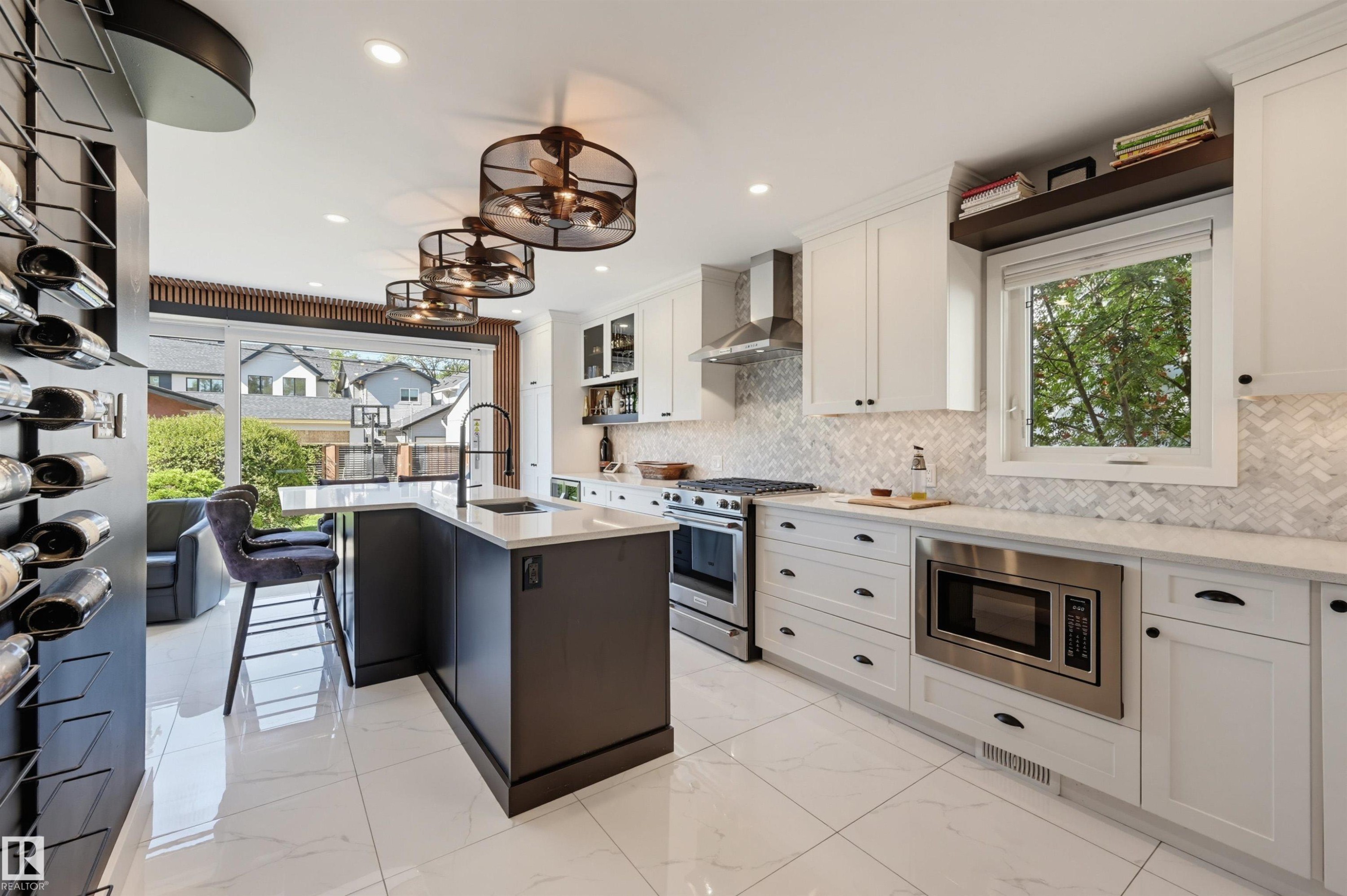 Modern kitchen featuring white shaker cabinetry, stainless steel appliances, a center island with a sink, and a herringbone-patterned backsplash - 10726 128 Street Nw, Edmonton, AB