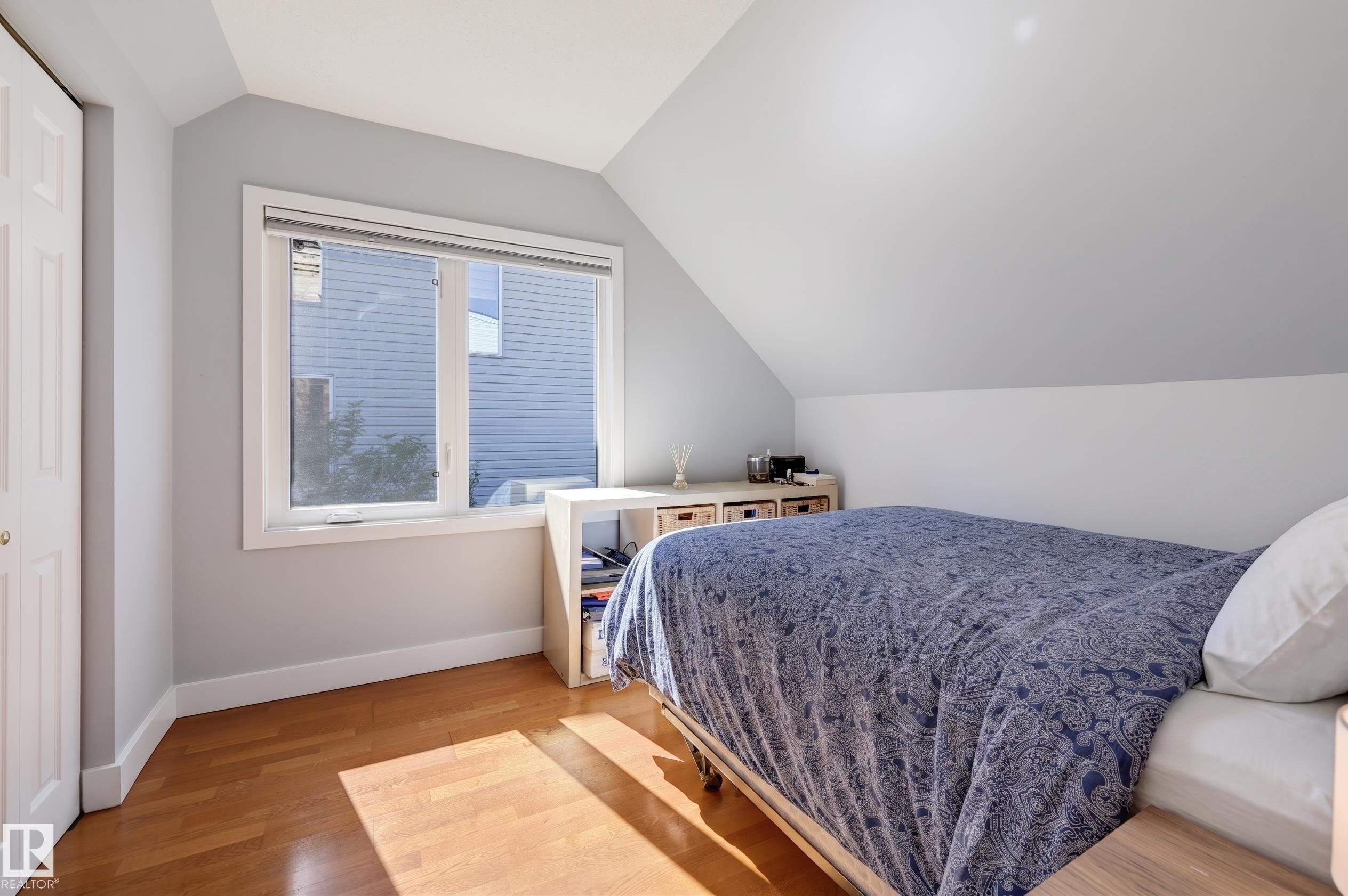 Sloped ceiling room featuring wood-finish flooring, a double window, and a white bi-fold closet door - 10726 128 Street Nw, Edmonton, AB
