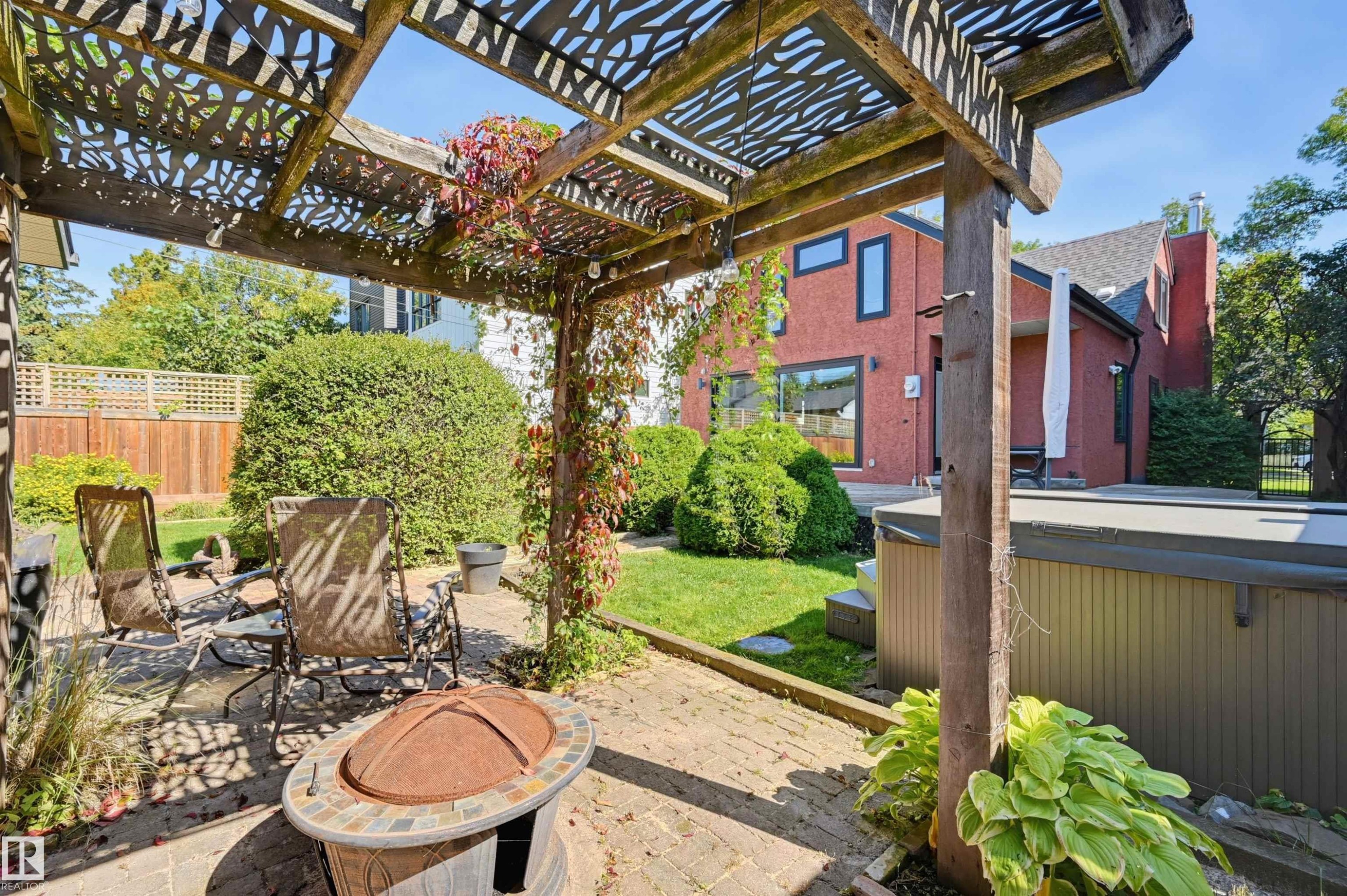 Backyard patio featuring a wood pergola with decorative cutouts, a hot tub, and a brick exterior structure - 10726 128 Street Nw, Edmonton, AB