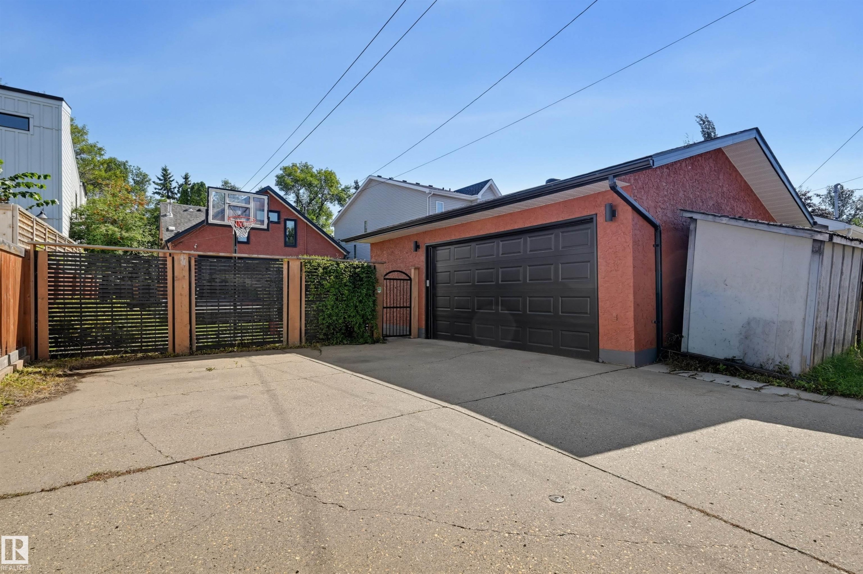 Detached garage with a black panel door, a side entry gate, and an attached storage shed - 10726 128 Street Nw, Edmonton, AB